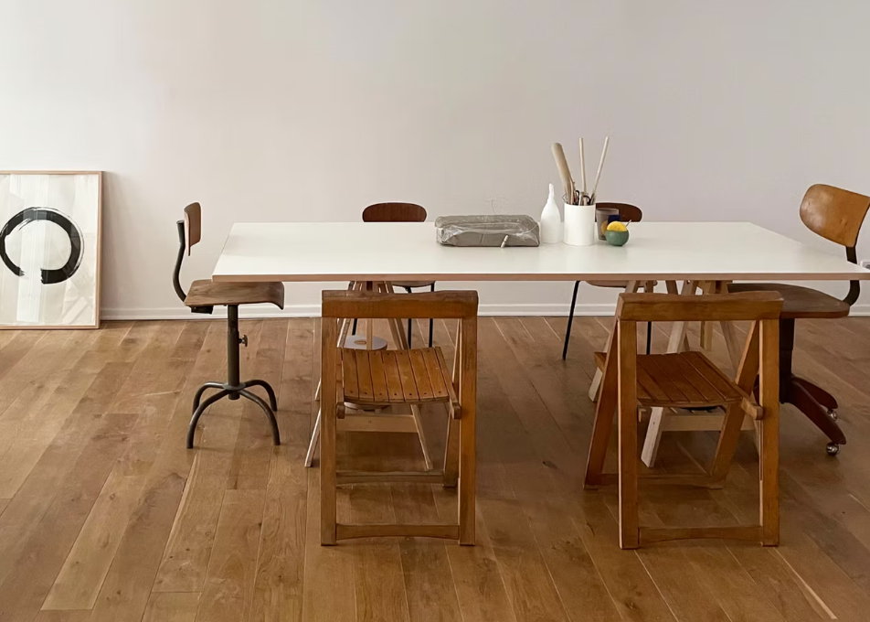 Dining area with wooden chairs and a white table against a plain wall.