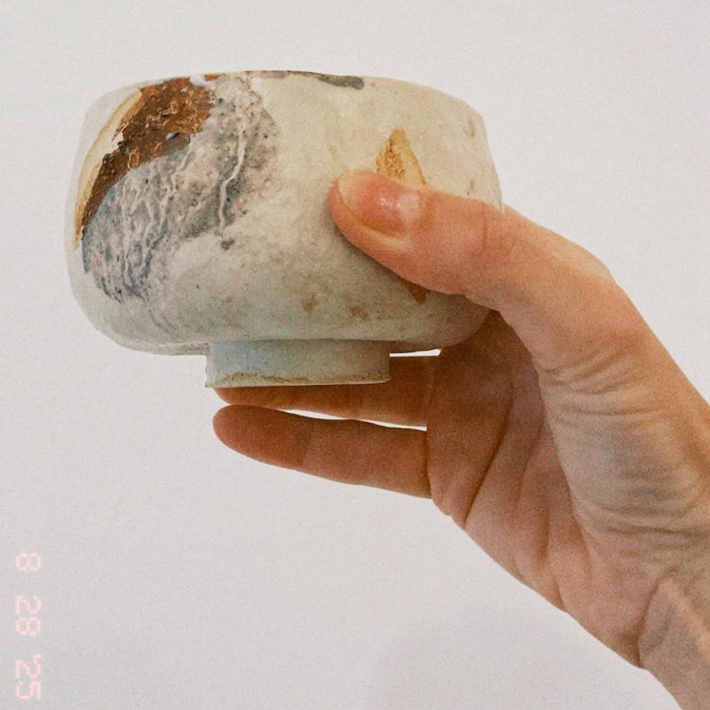 Hand holding a small ceramic bowl with a textured surface against a plain background