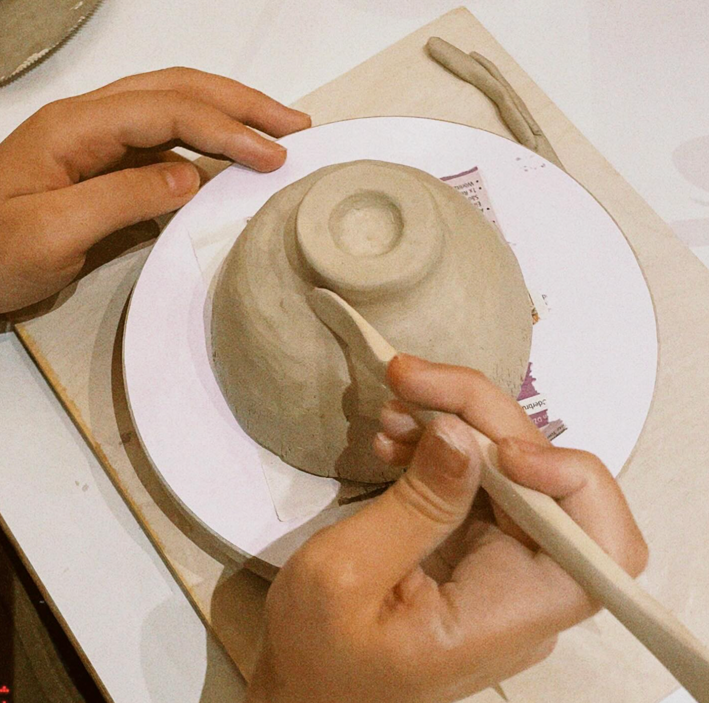 Person working on a ceramic piece with a wooden tool on a white surface