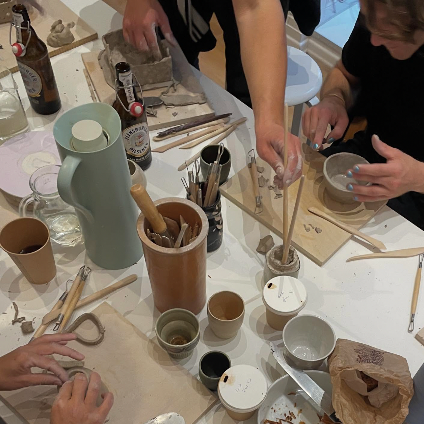 People working on pottery at a table with various ceramic items and tools.