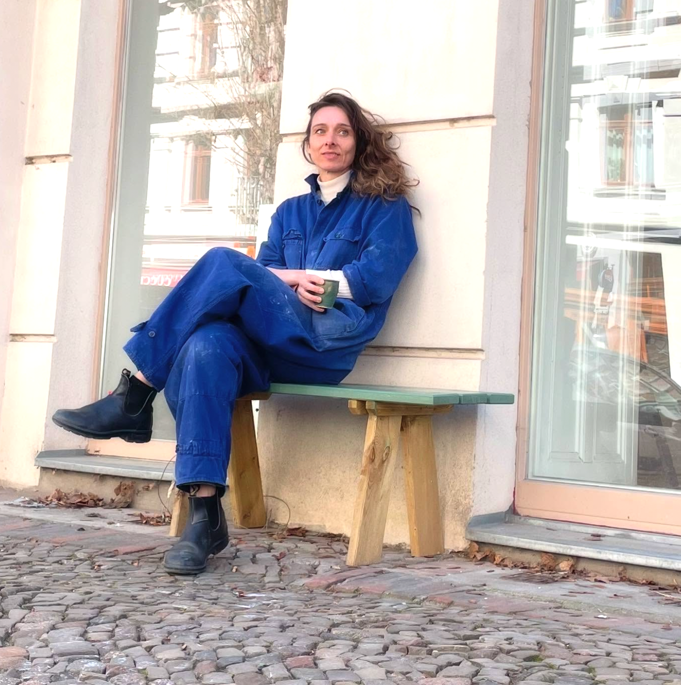 Person wearing a blue jumpsuit sitting on a bench outside a building.