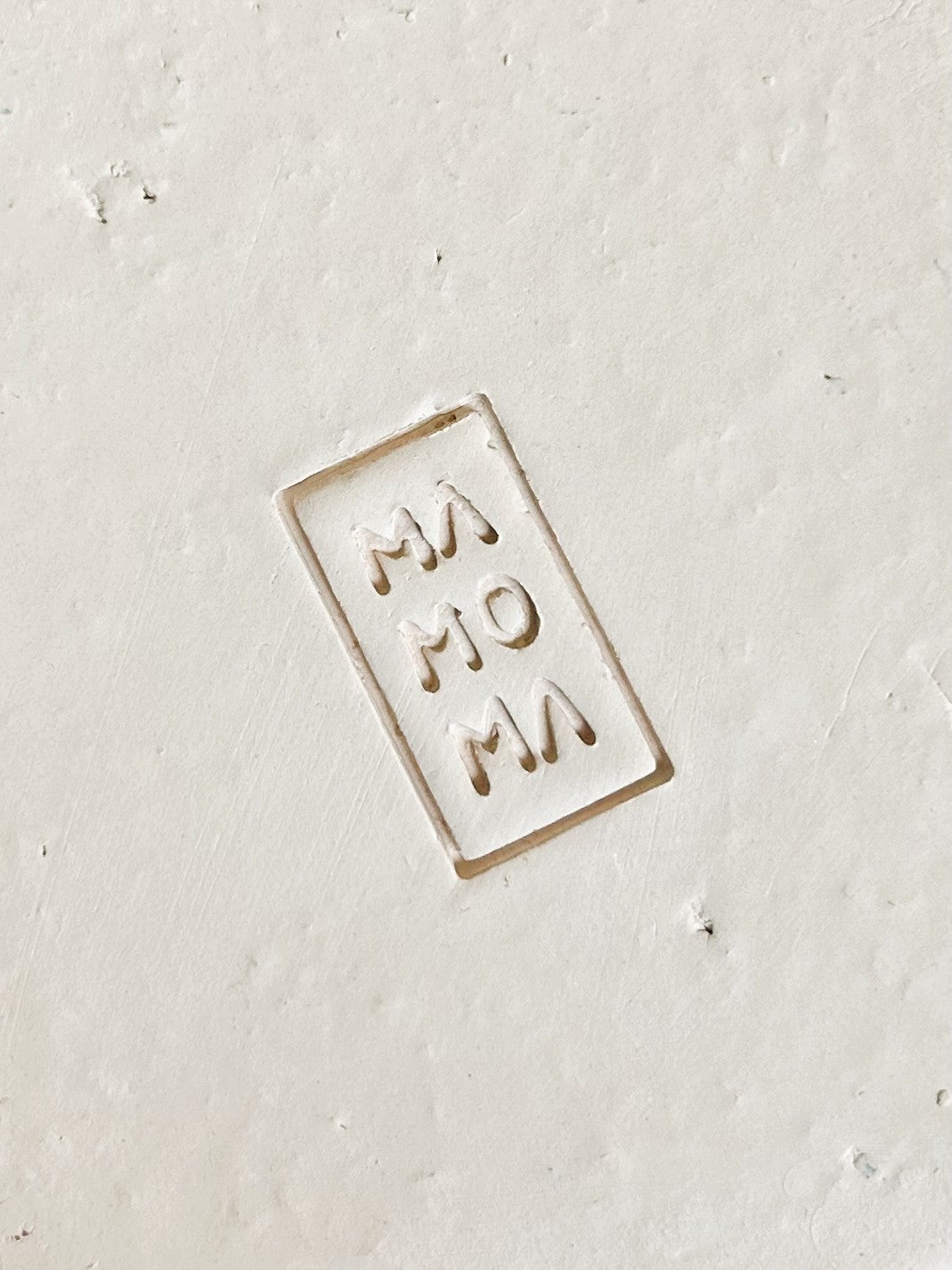Small rectangular ceramic stamp with 'MOM' text on a light gray background