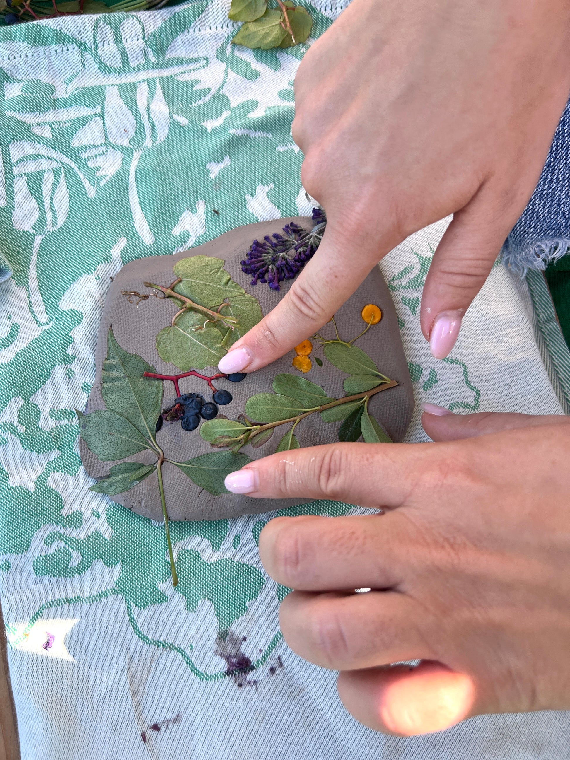 Handmade decorative stone with pressed flowers and leaves on a green fabric background