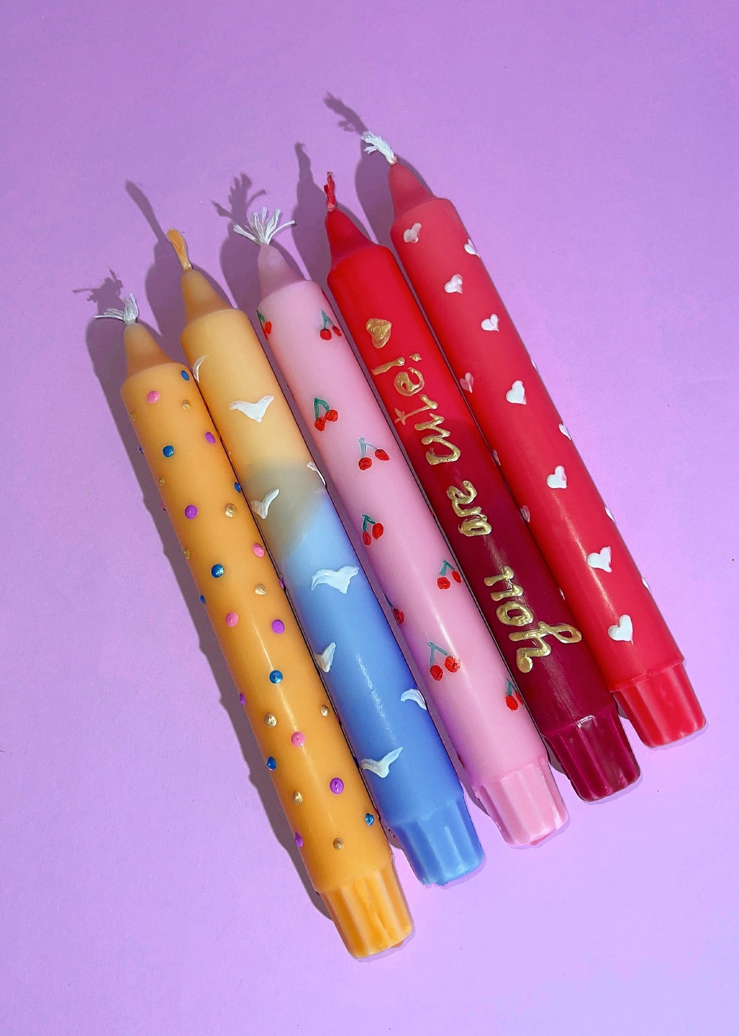 Set of colorful candles with decorative text and designs on a pink background