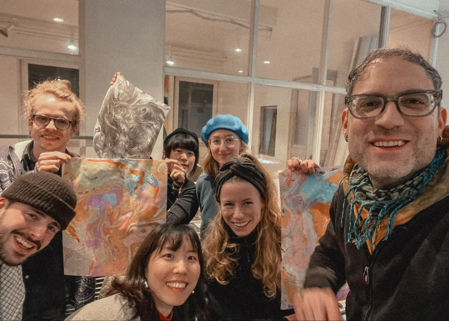 Group of people posing with a colorful painting indoors.
