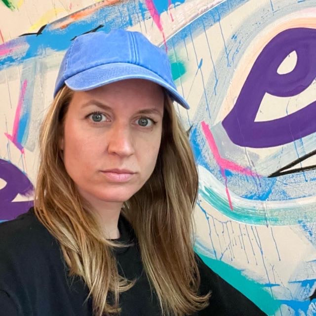 Person wearing a blue cap in front of a colorful abstract painting