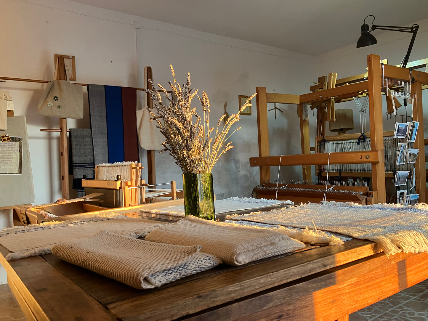 Room with wooden tables, woven items, and a vase with dried plants.