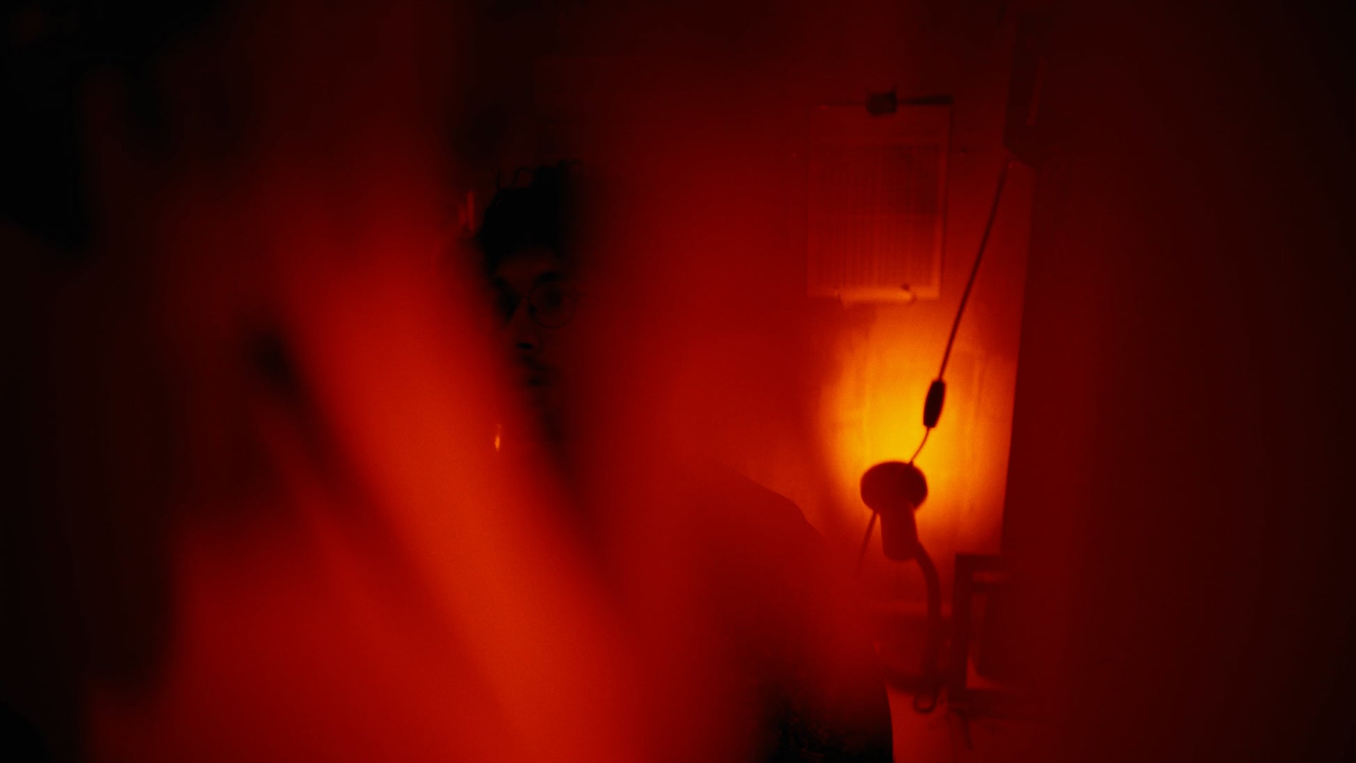 A dimly lit scene dominated by intense red and orange light, with a dark silhouette of a person holding a phone receiver in a dark interior.