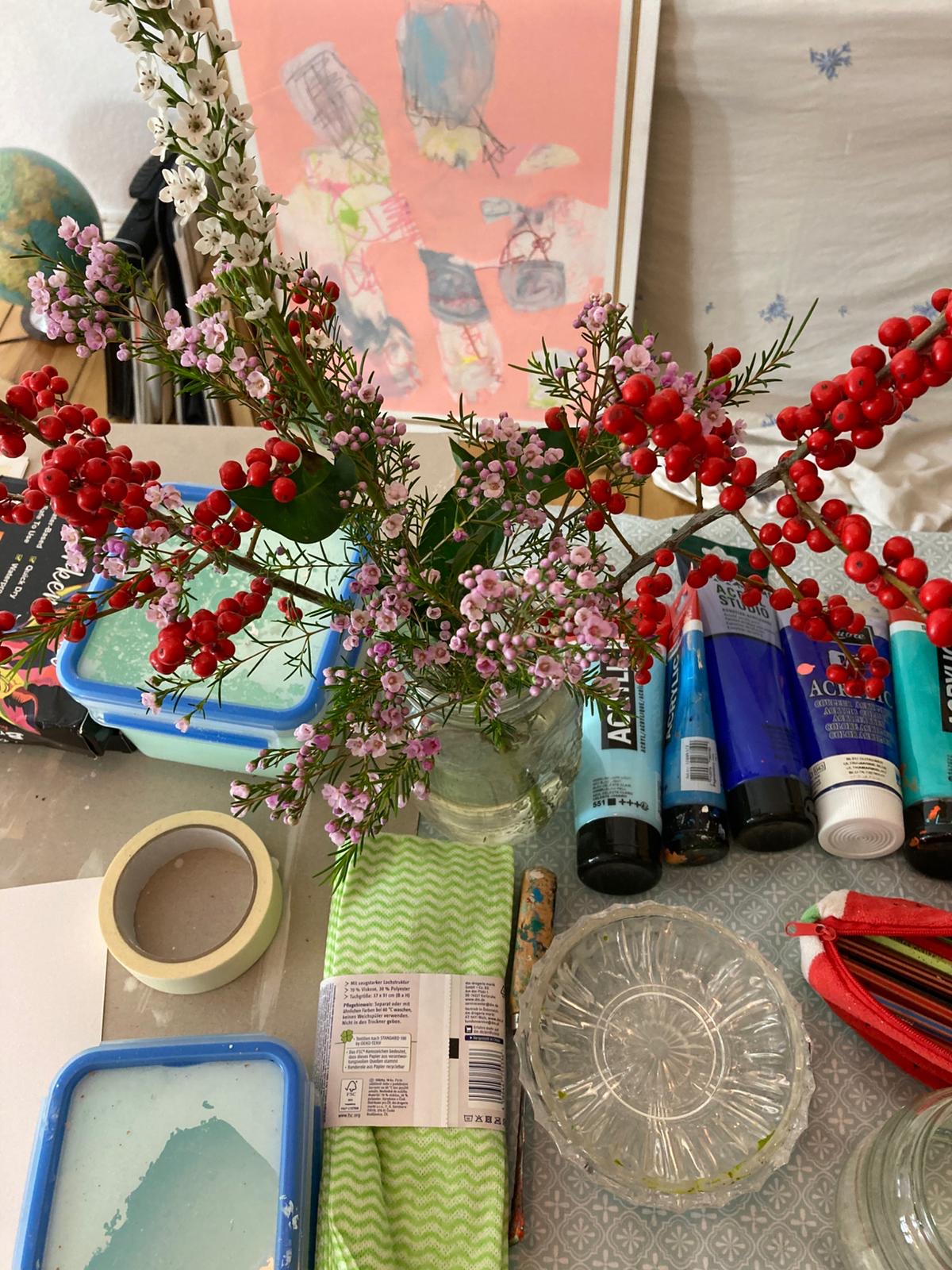 Bouquet of flowers with red berries on a cluttered desk with stationery items.