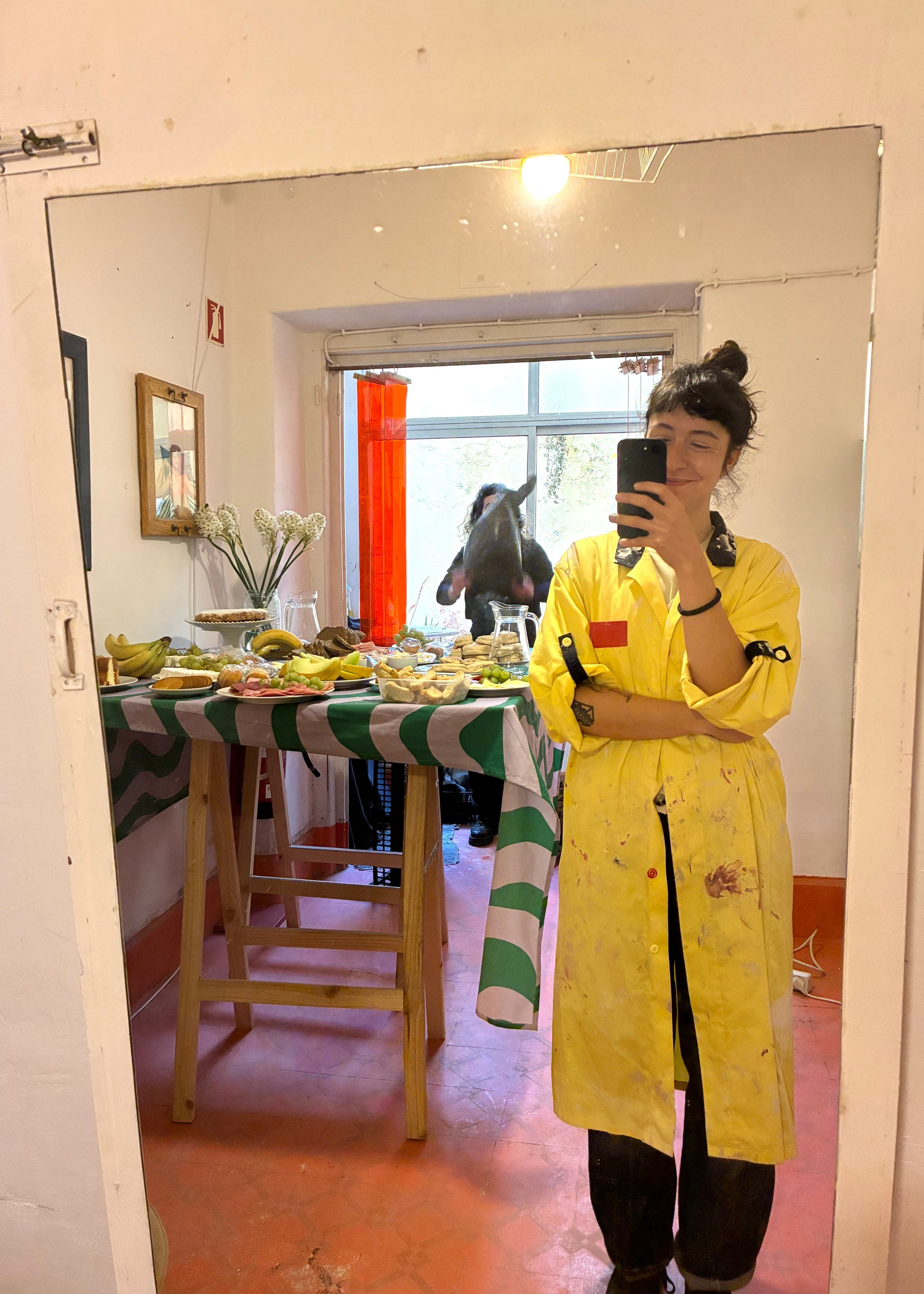 Person taking a mirror selfie wearing a yellow raincoat in a room with a table and decor.