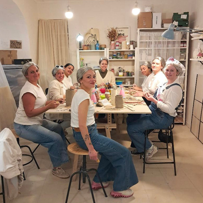 Group of women sitting around a table in a room with shelves and decor.