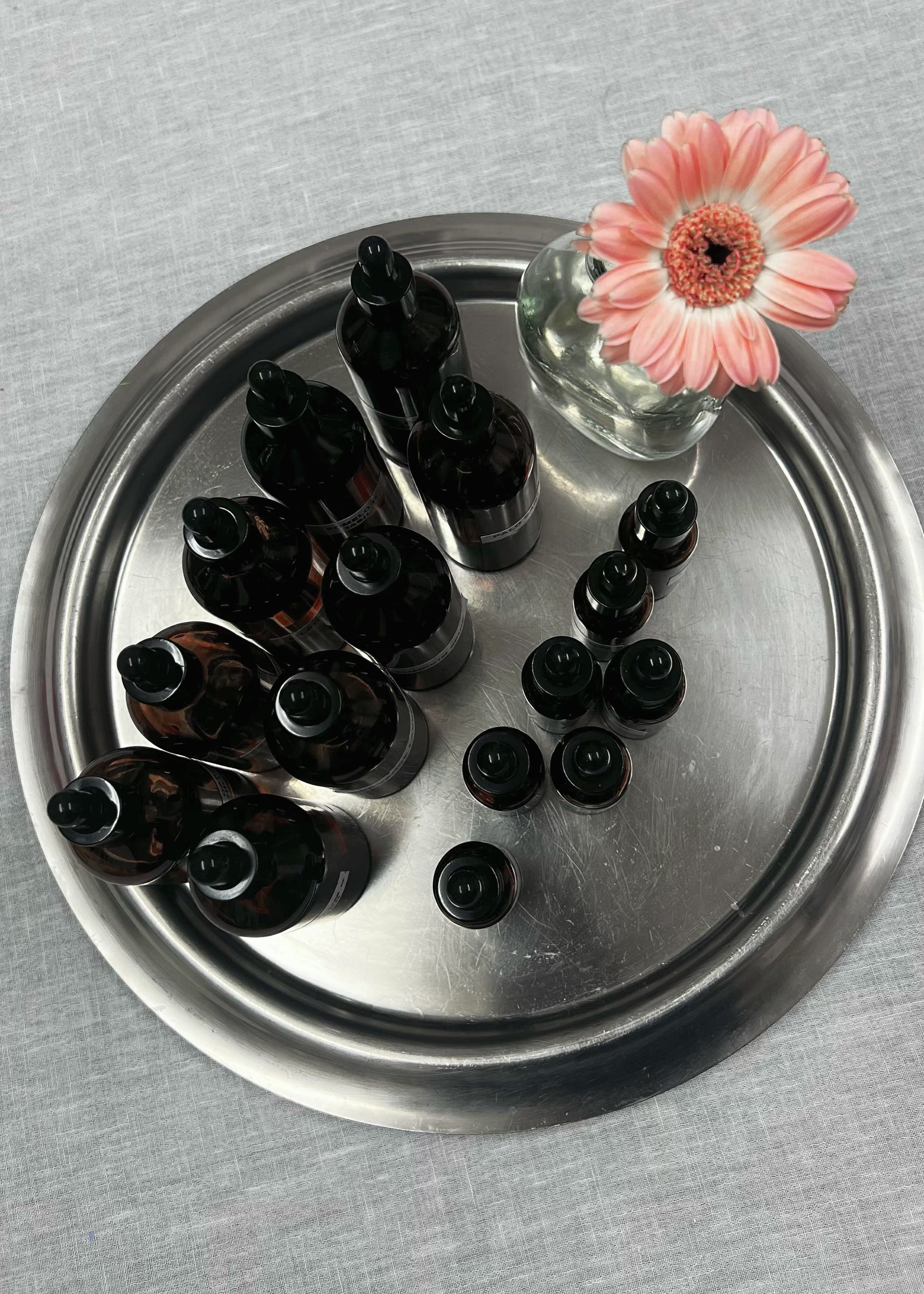 Set of dark glass bottles on a metal tray with a pink flower on a gray surface