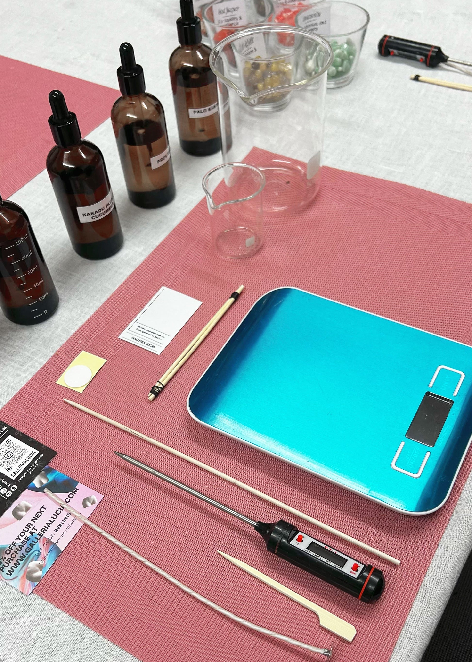 Table with various items including bottles, a blue digital scale, and tools on a red mat.