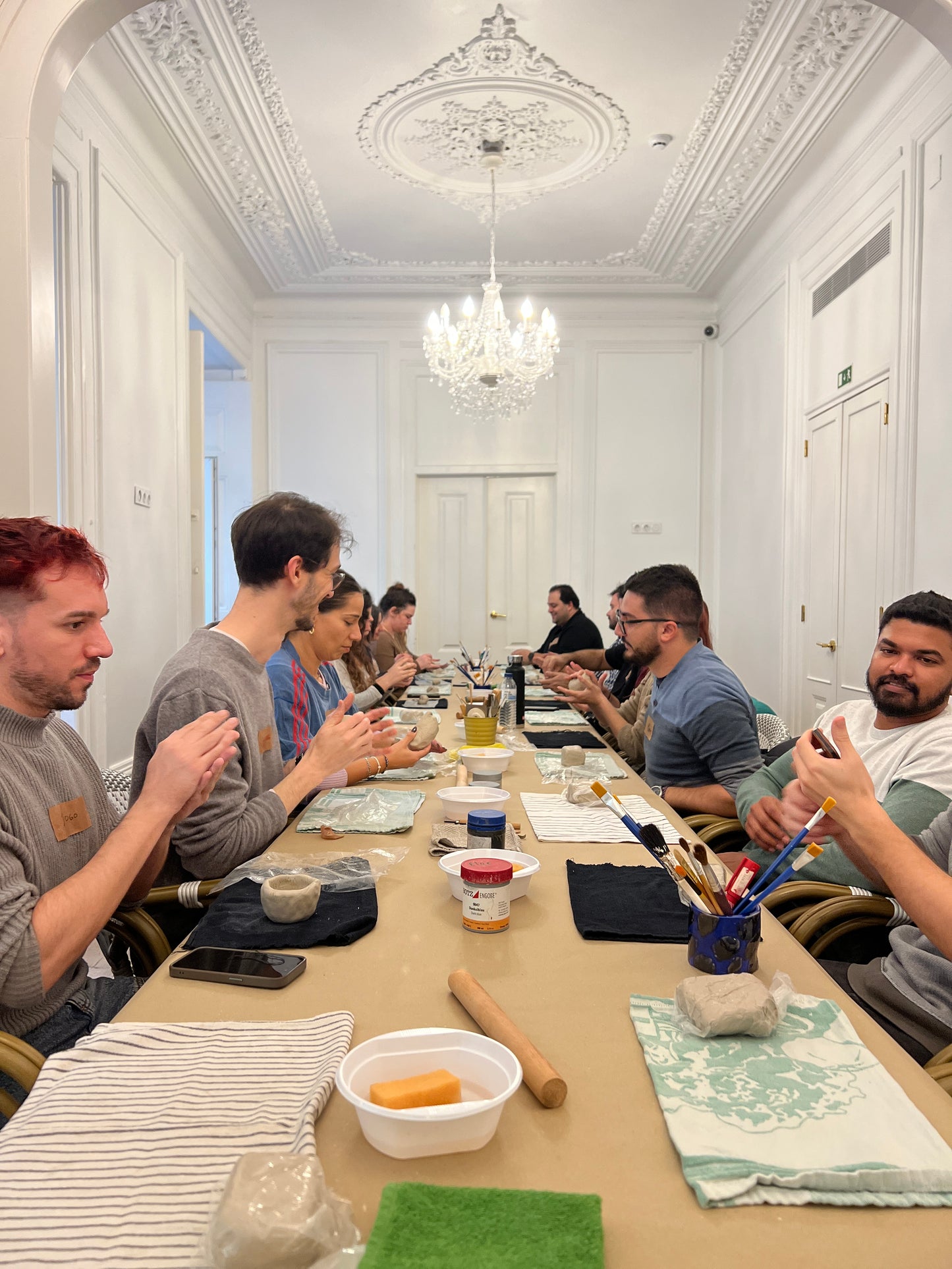 People gathered around a table in a room with decorative ceiling and chandelier.