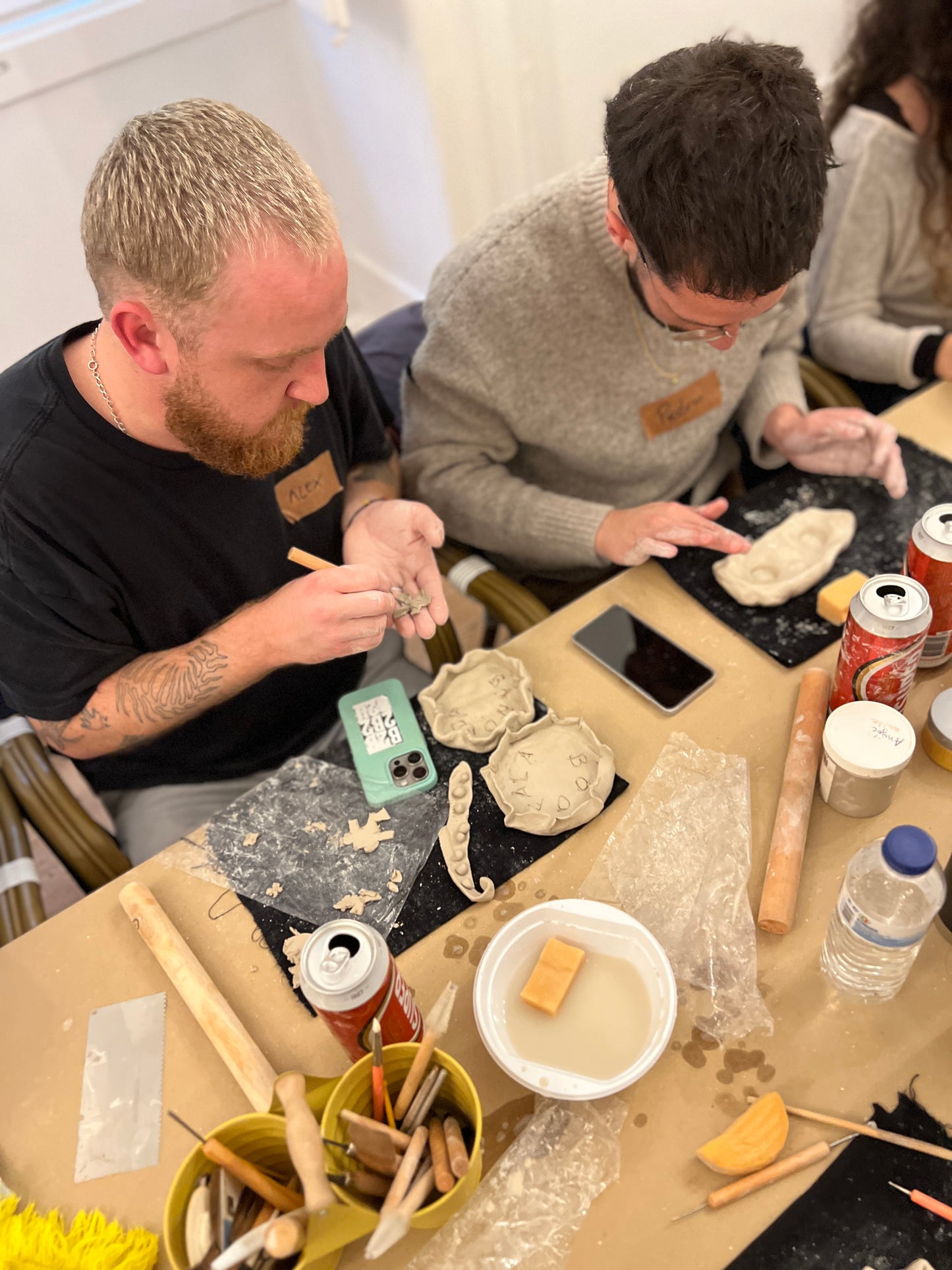 Two men working with clay at a table in a workshop setting.