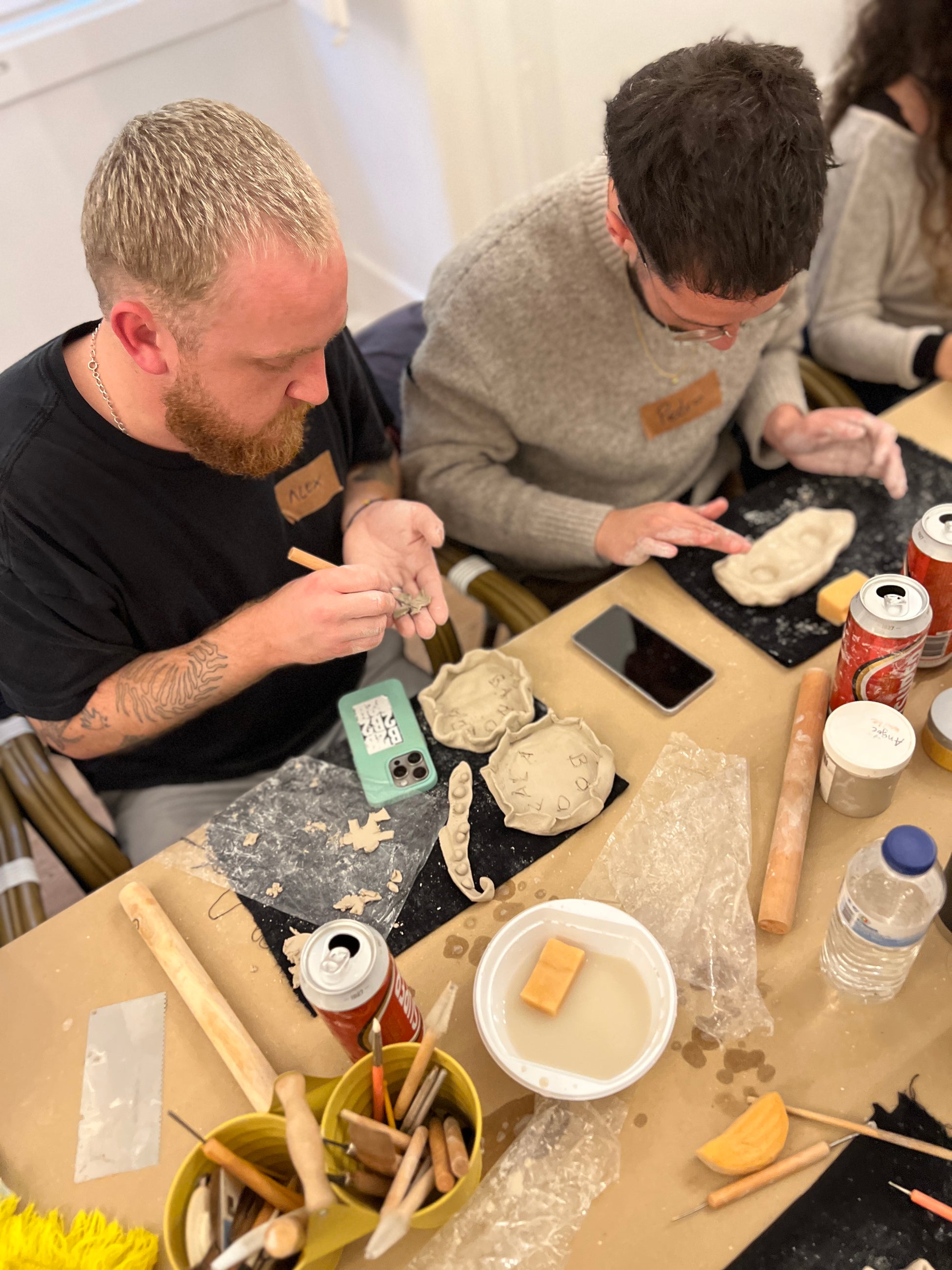 Two men working with clay at a table in a workshop setting.