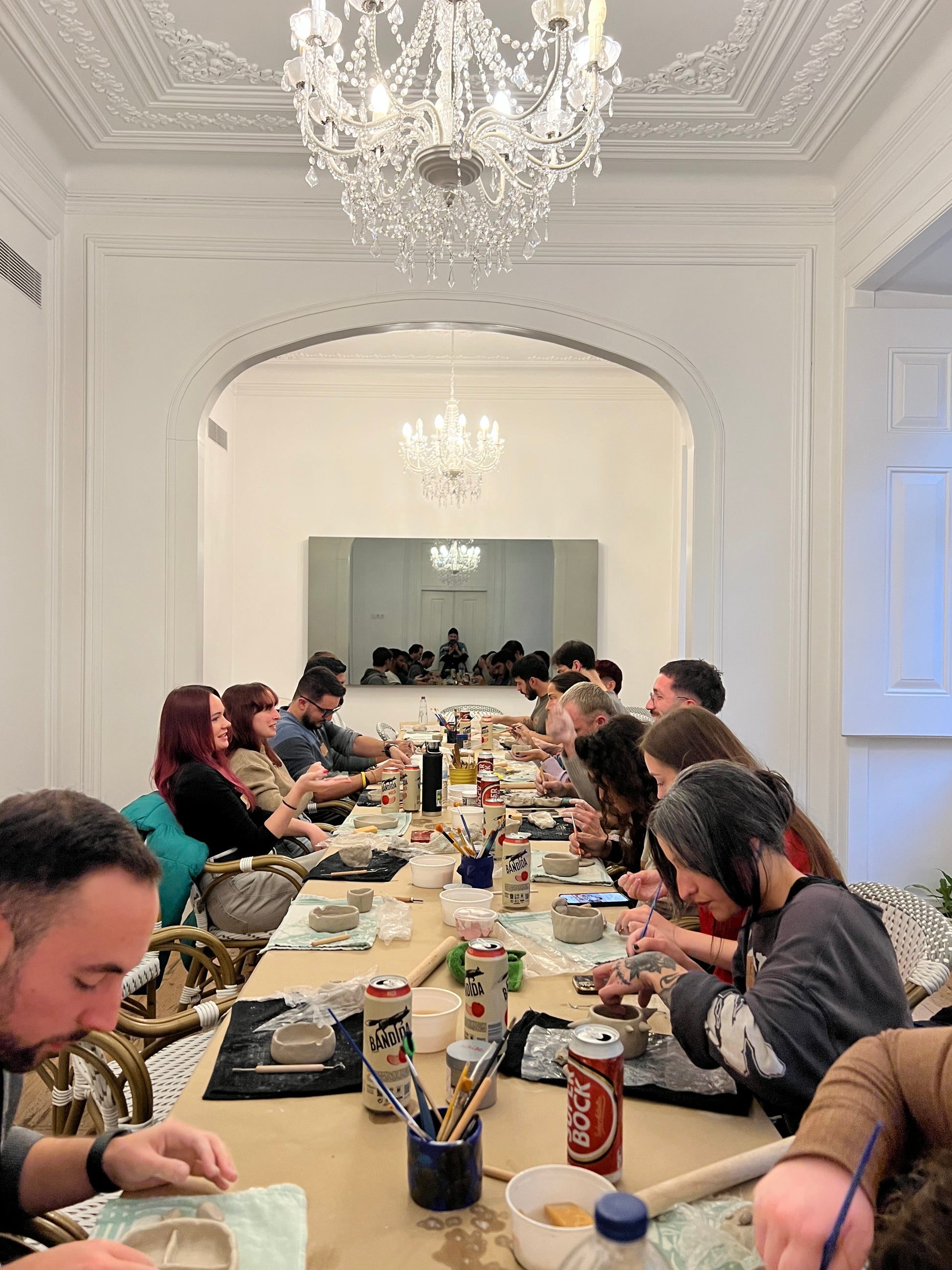 Group of people sitting around a long dining table in an elegant room with chandeliers.