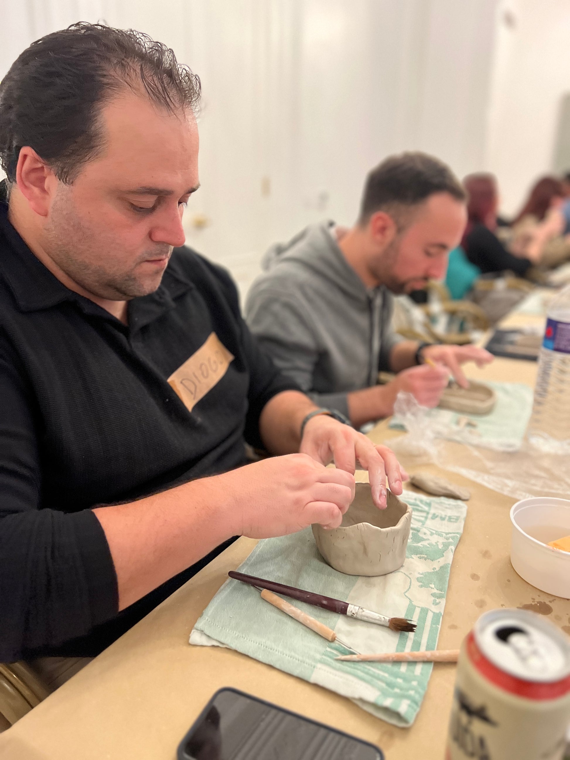 Man working with clay at a pottery workshop, surrounded by tools and materials.