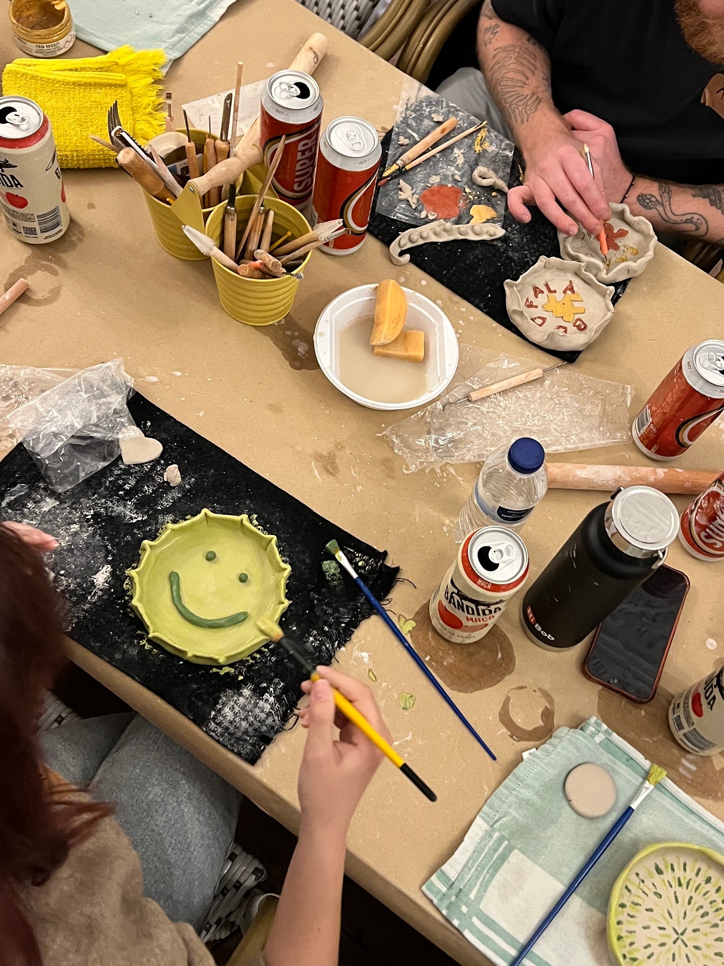 Table with ceramic art projects, drinks, and people working on them