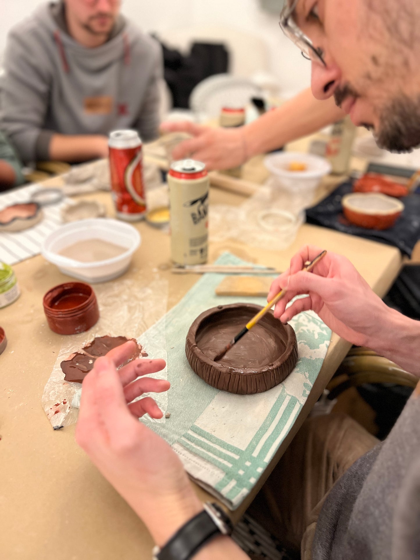 Person working with clay on a table with various items including cans and bowls.