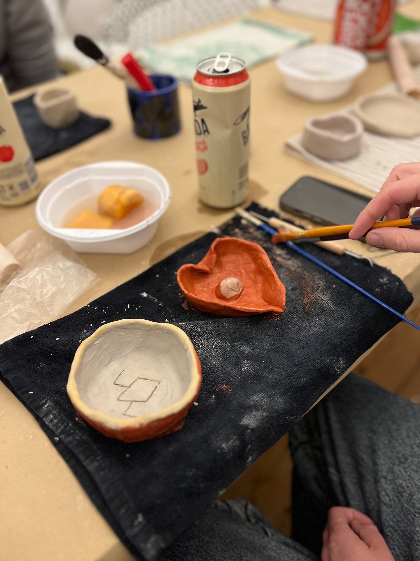 Ceramic bowls on a table with a person using a tool, surrounded by various items including a can.
