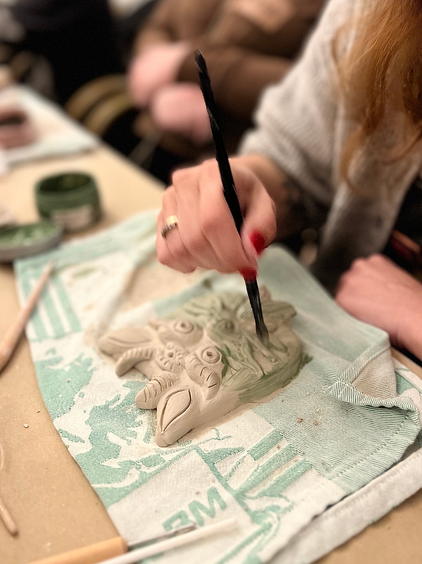 Person painting a ceramic frog sculpture on a textured surface.