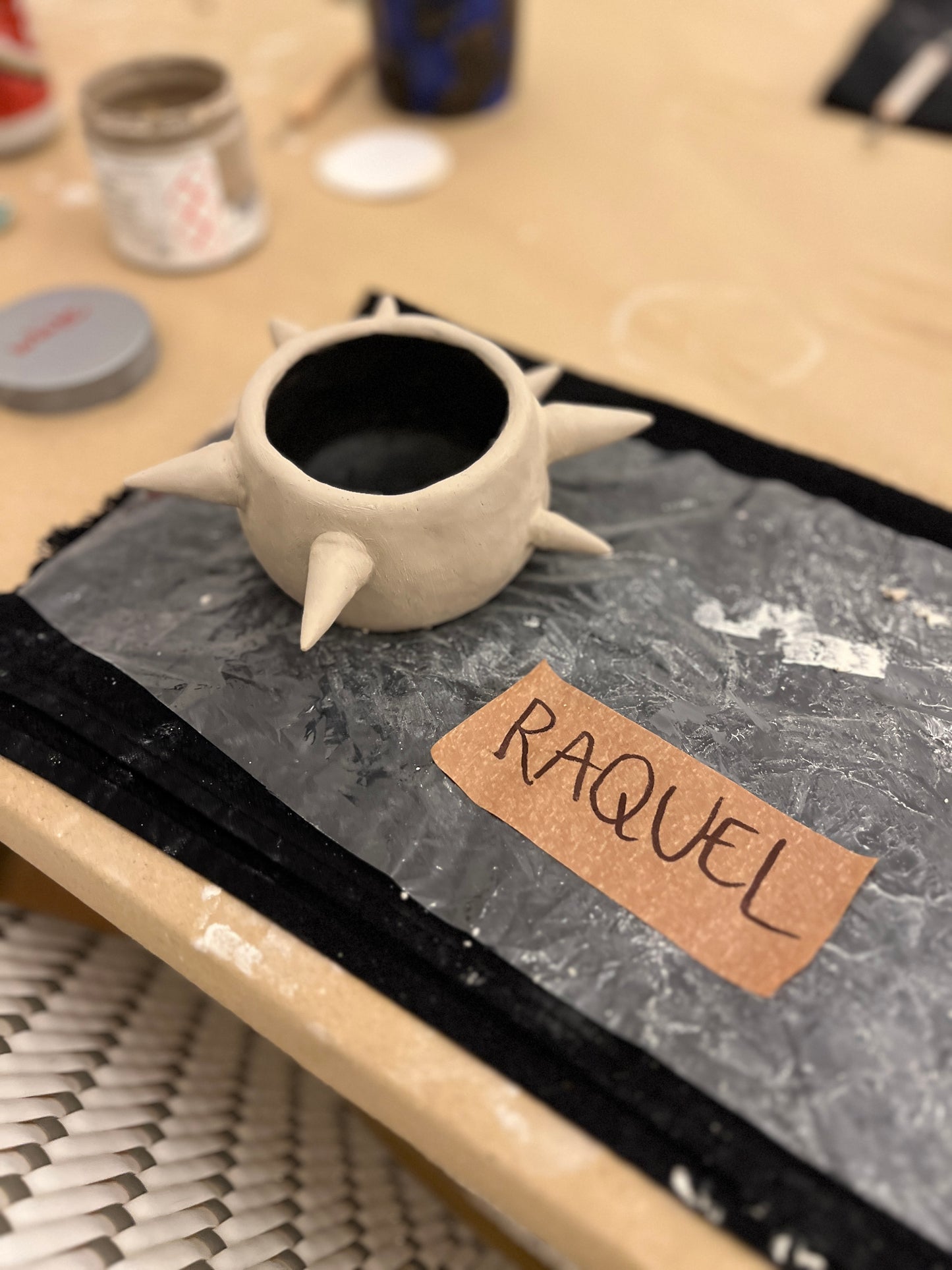 Ceramic mug with spiky design on a table with 'RAQUEL' label