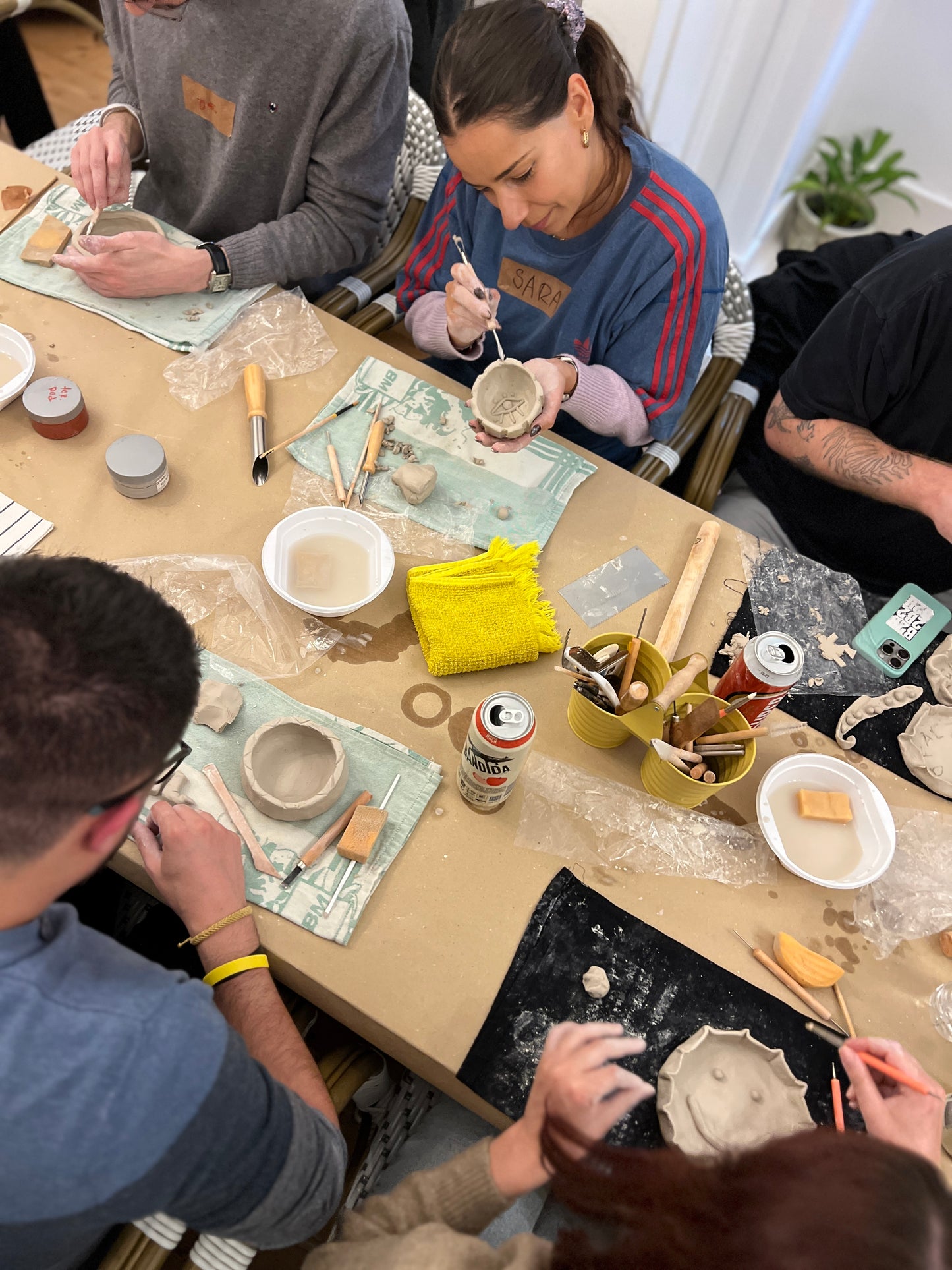 Group of people working on pottery at a table with various tools and materials.