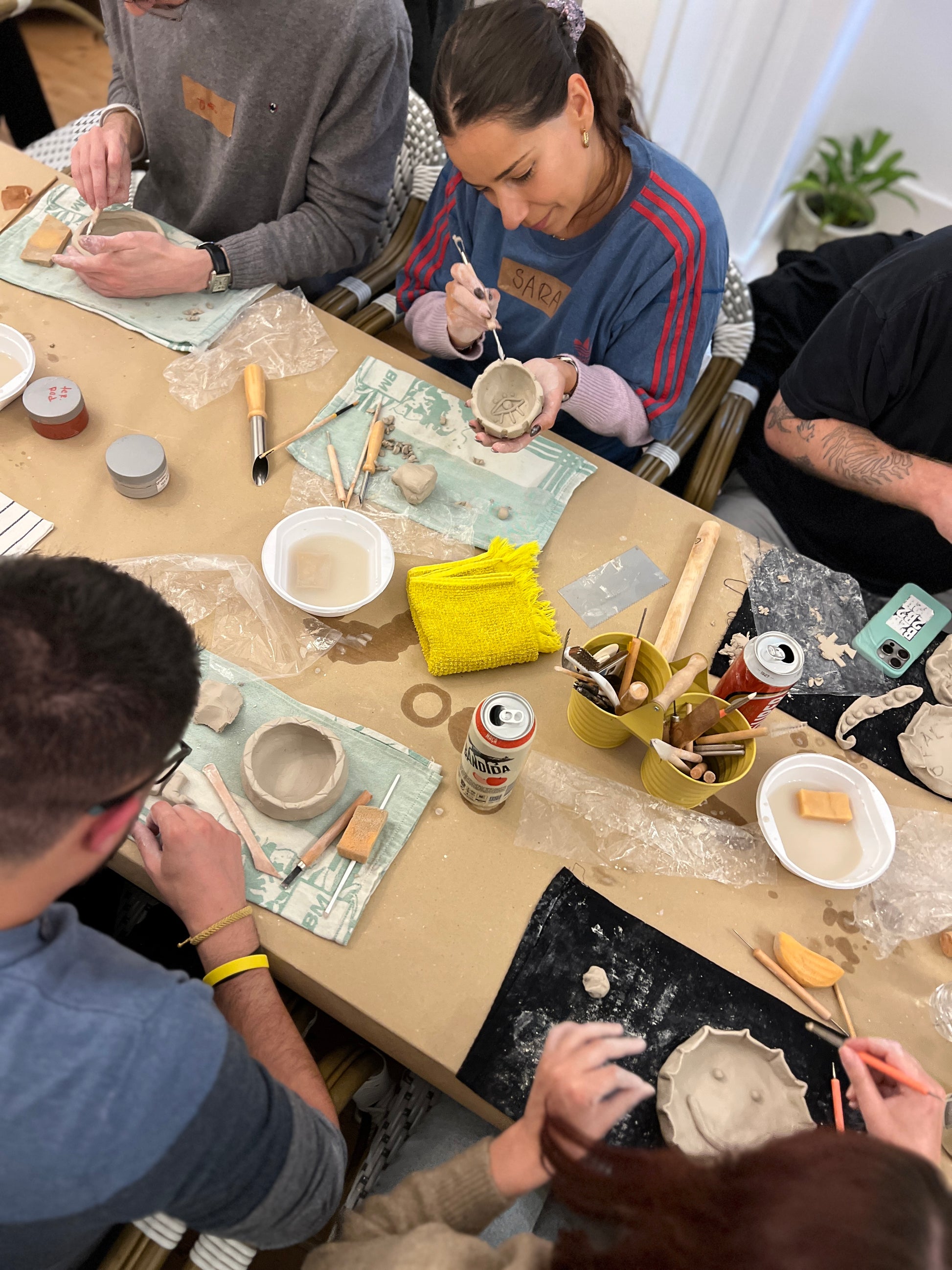 Group of people working on pottery at a table with various tools and materials.
