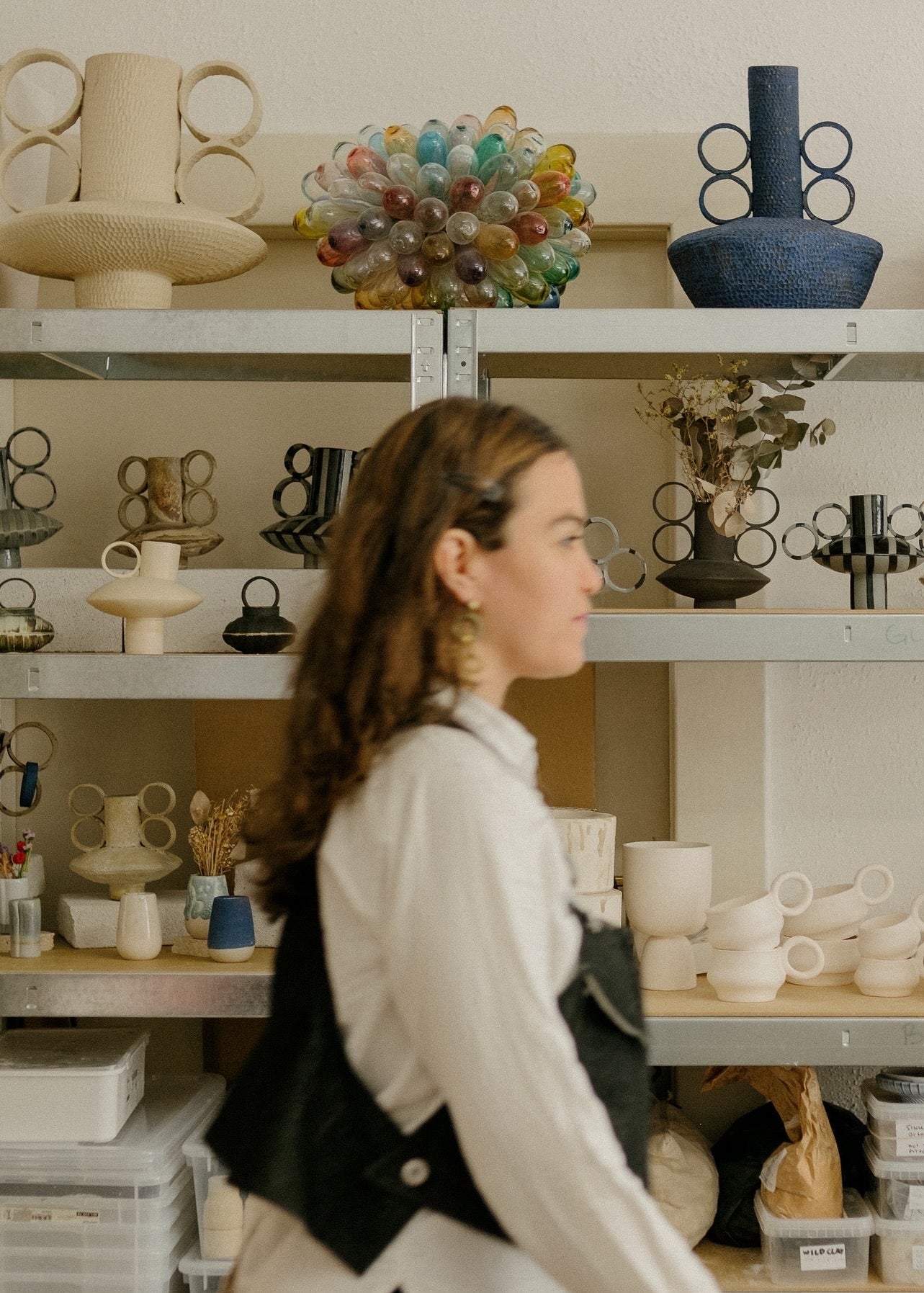Woman walking past shelves displaying various ceramic and glass art pieces in a store.