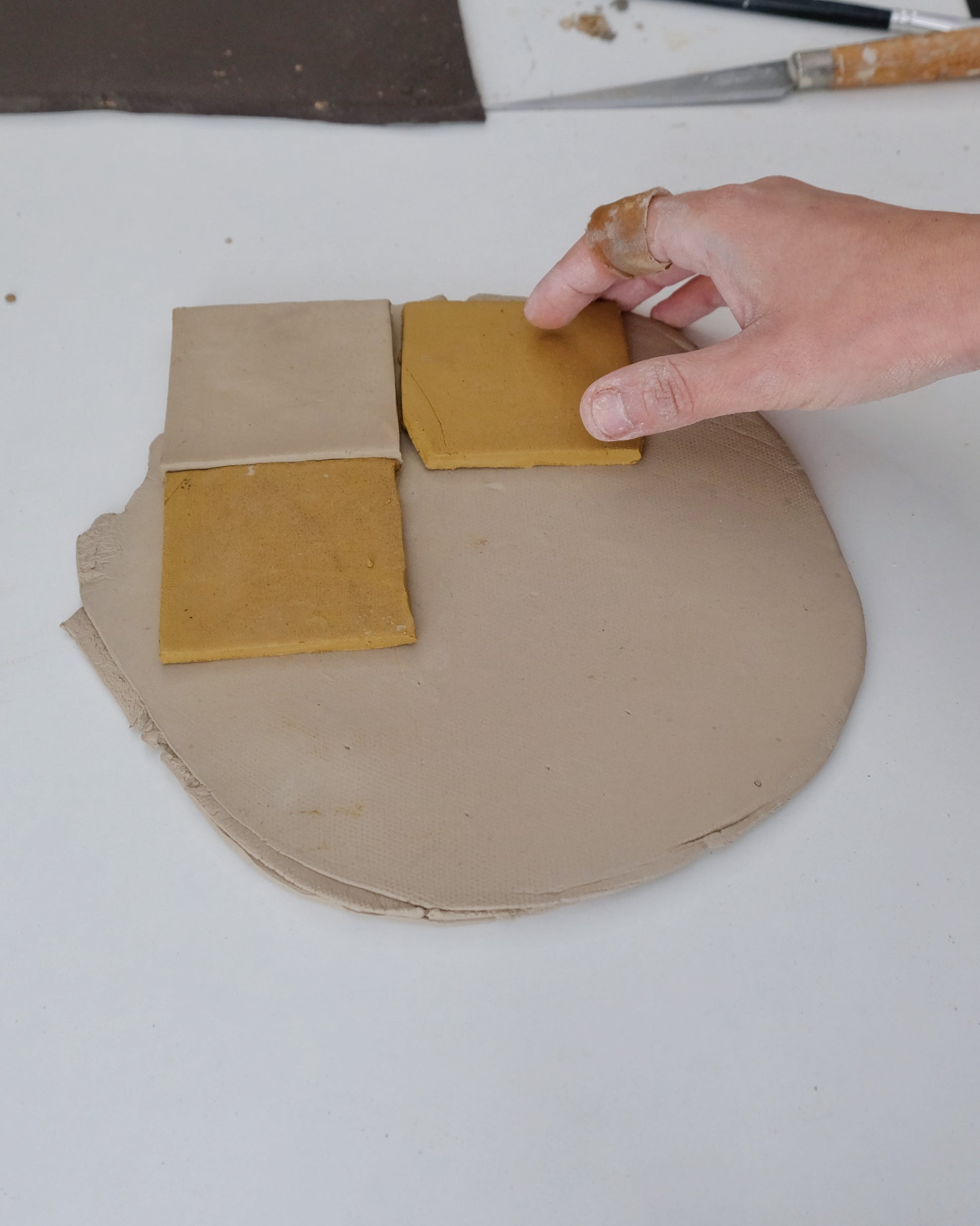Hand arranging square pieces of beige and yellow material on a circular beige base.