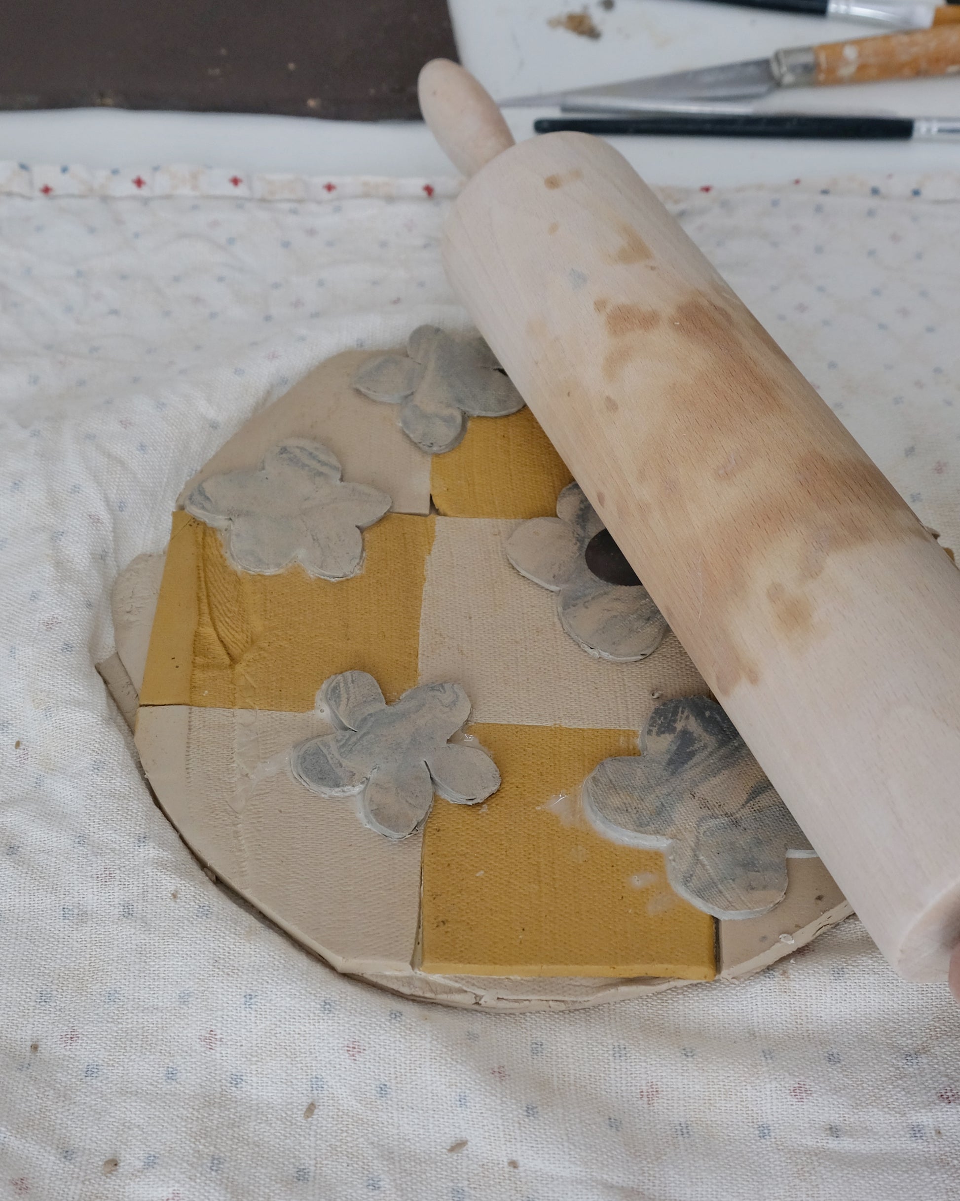 Rolling pin pressing into a decorative wooden wheel with floral patterns on a white fabric background.