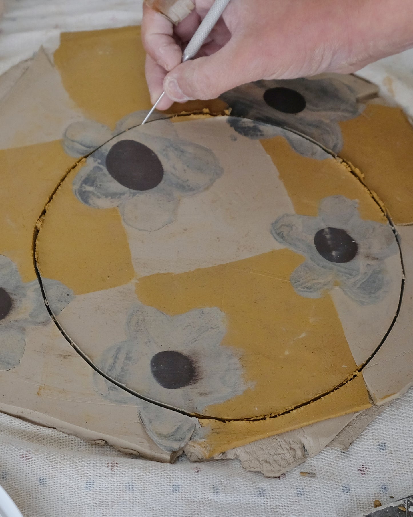 Person painting a floral design on a yellow circular object with a brush.
