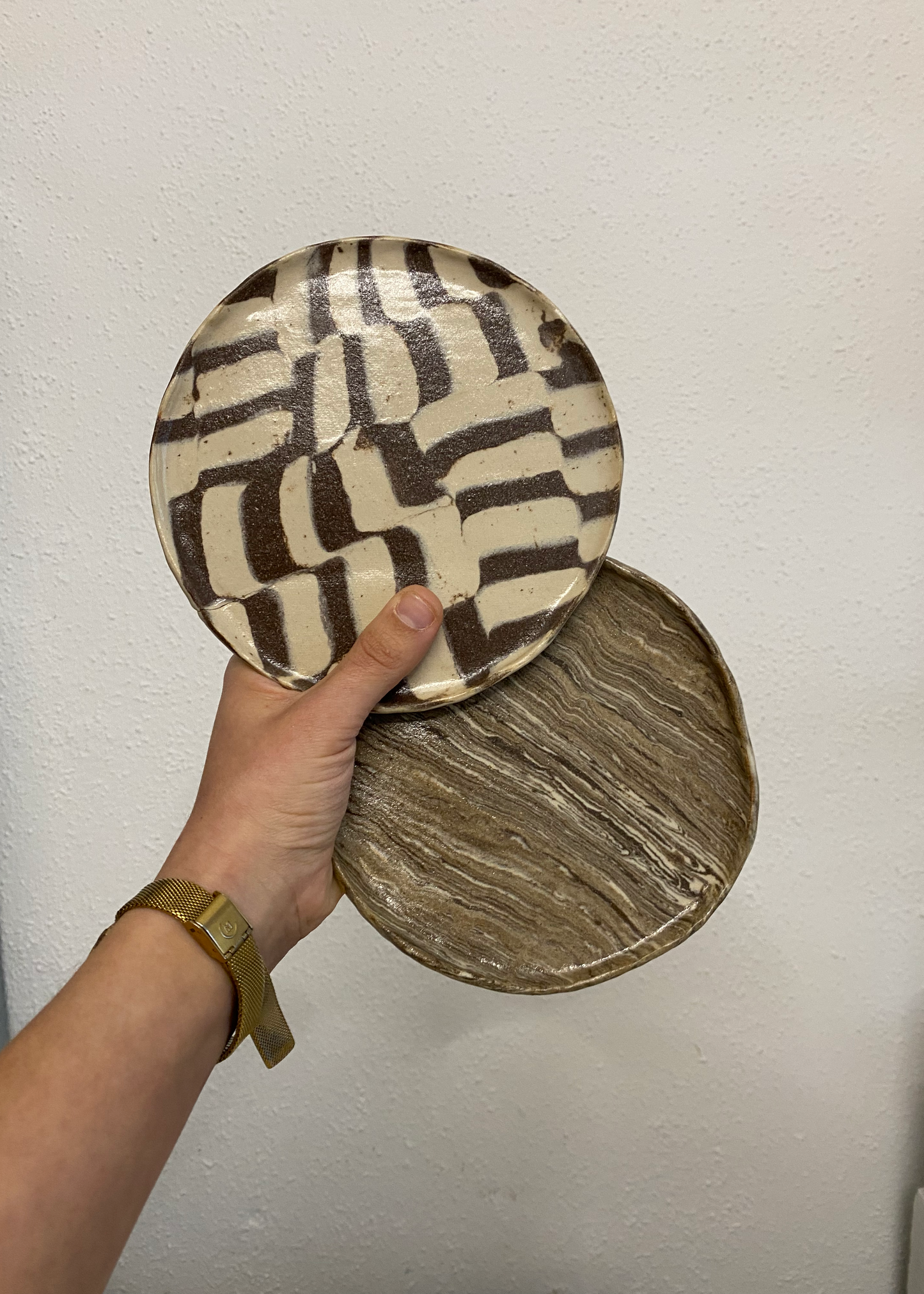 Hand holding two ceramic plates with geometric patterns against a plain background