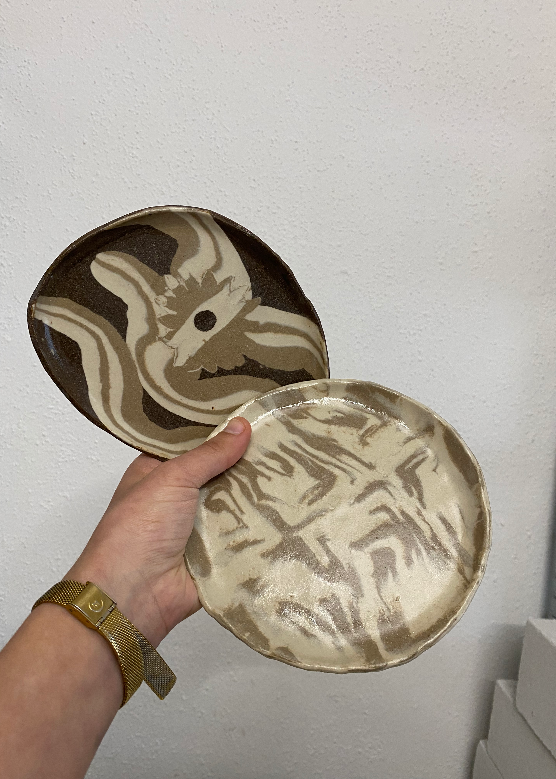 Ceramic plates with artistic designs held by a hand against a plain background