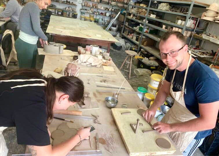 People working in a pottery studio with tools and materials on tables.