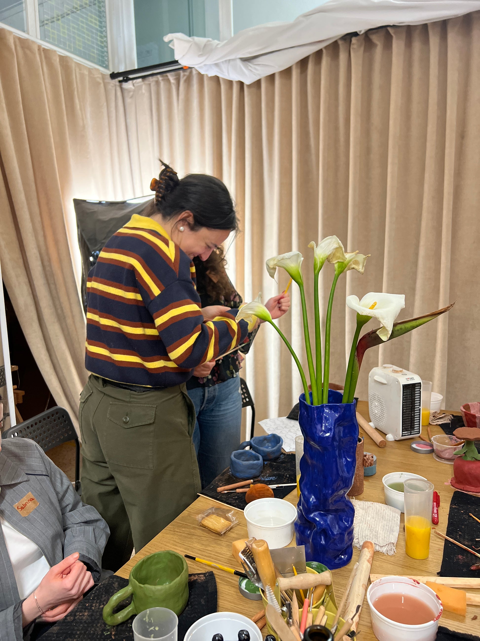 Person arranging flowers in a vase on a table with various items around