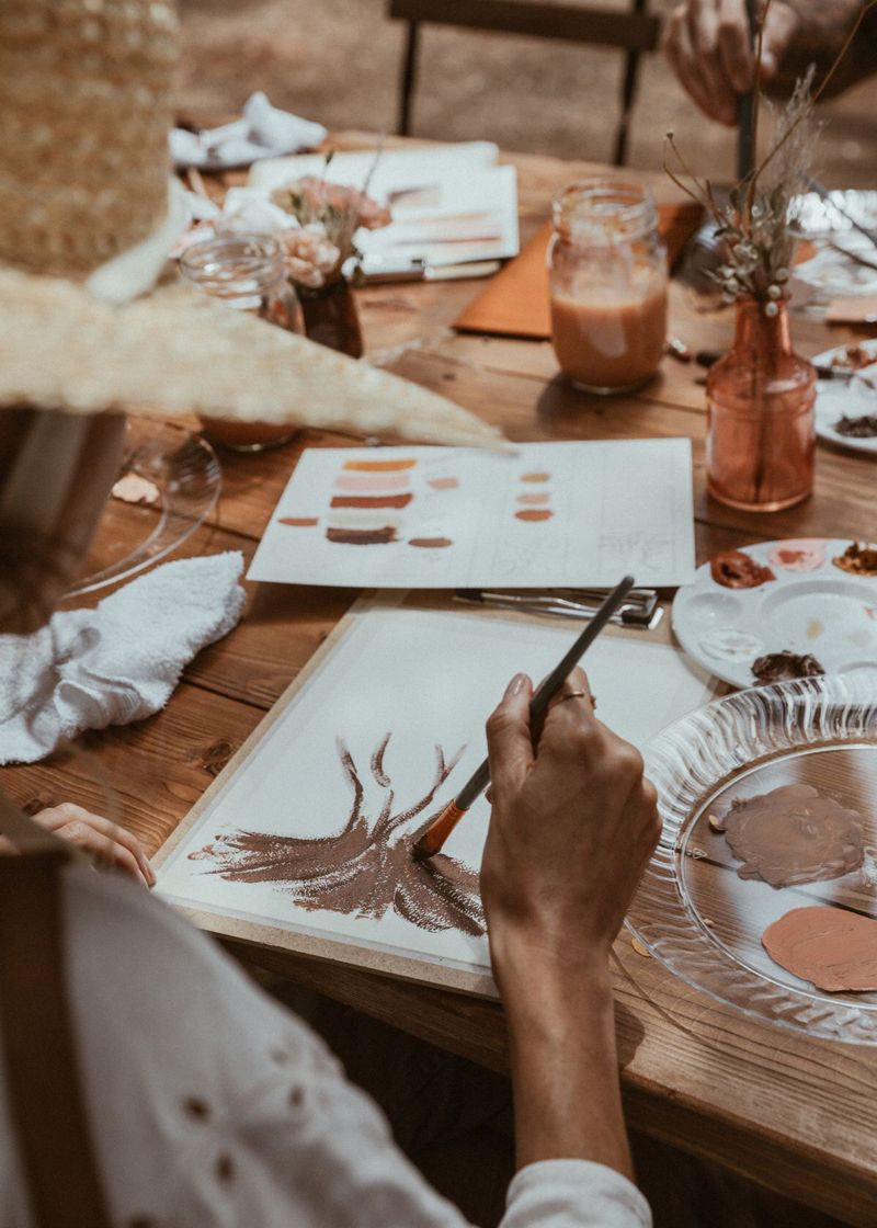 Person painting on a canvas at a table with art supplies