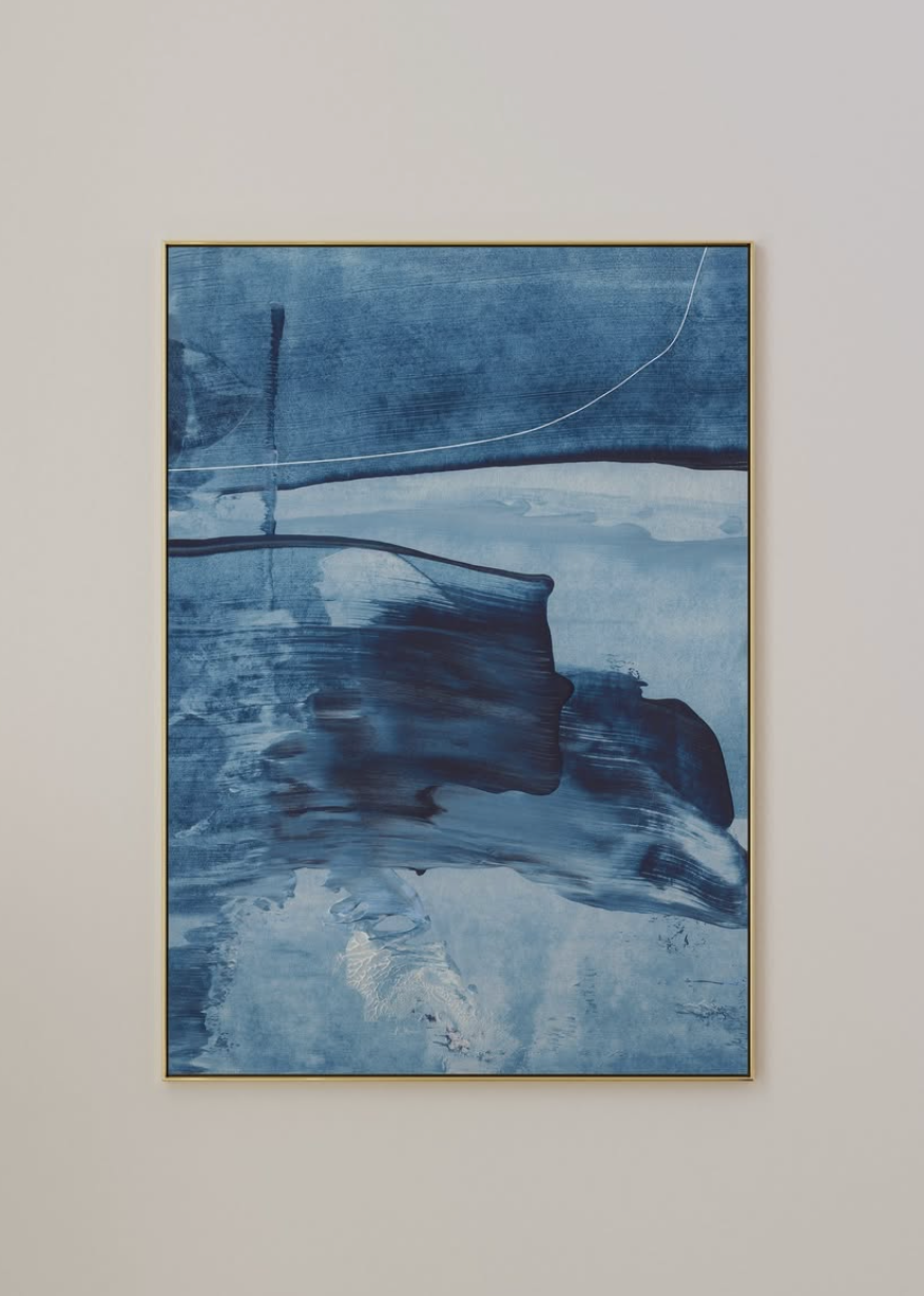 An abstract blue painting with textured brushstrokes and a thin gold frame, displayed on a light beige wall.