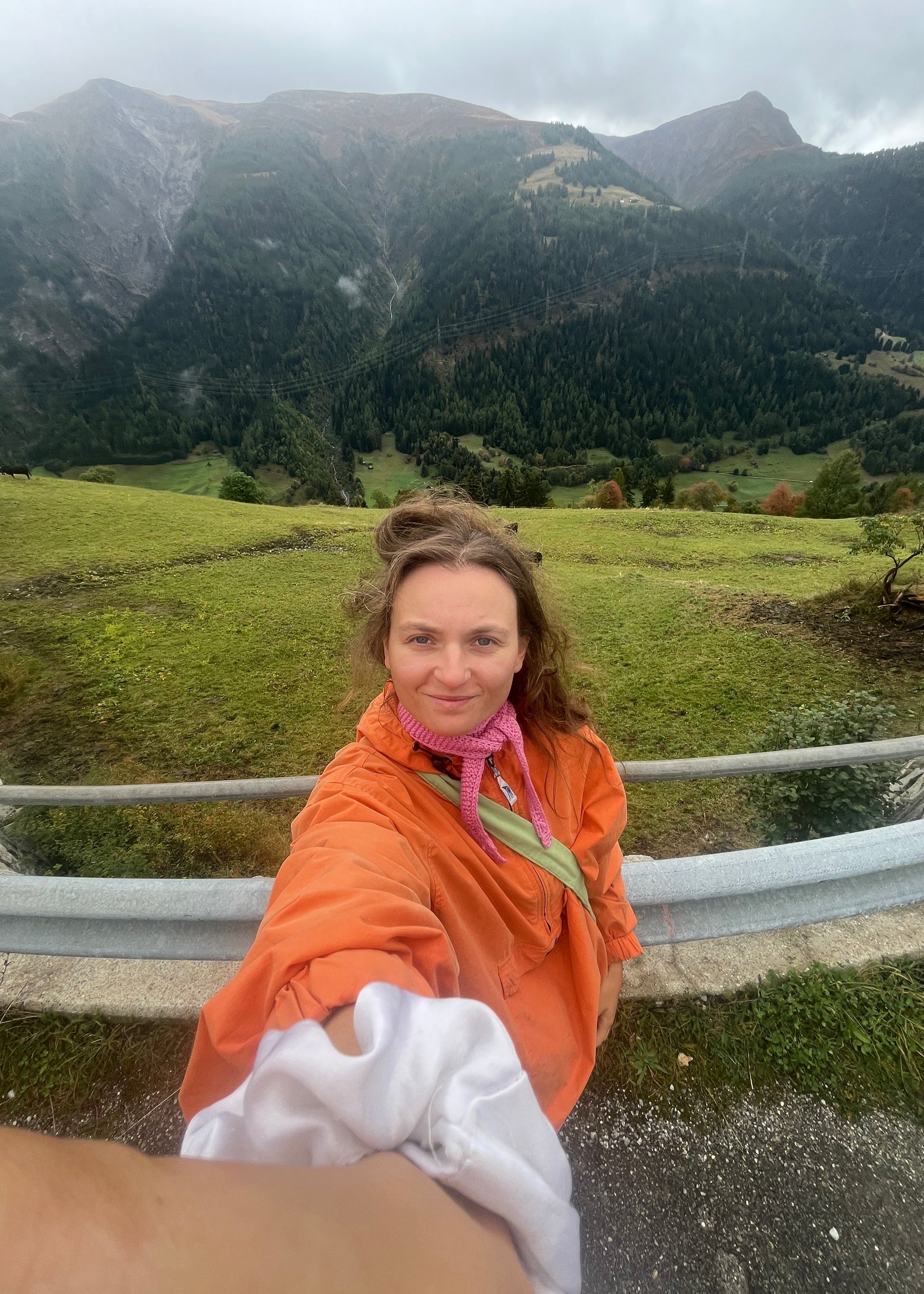 Person in an orange jacket standing by a road with mountains in the background