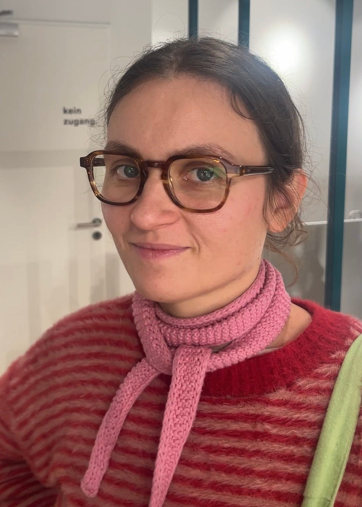 Person wearing a red striped sweater with a pink knitted scarf in an indoor setting