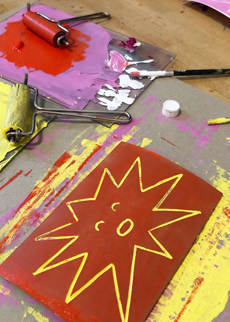 Artistic painting process with a sun design on a canvas, paint rollers, and brushes.