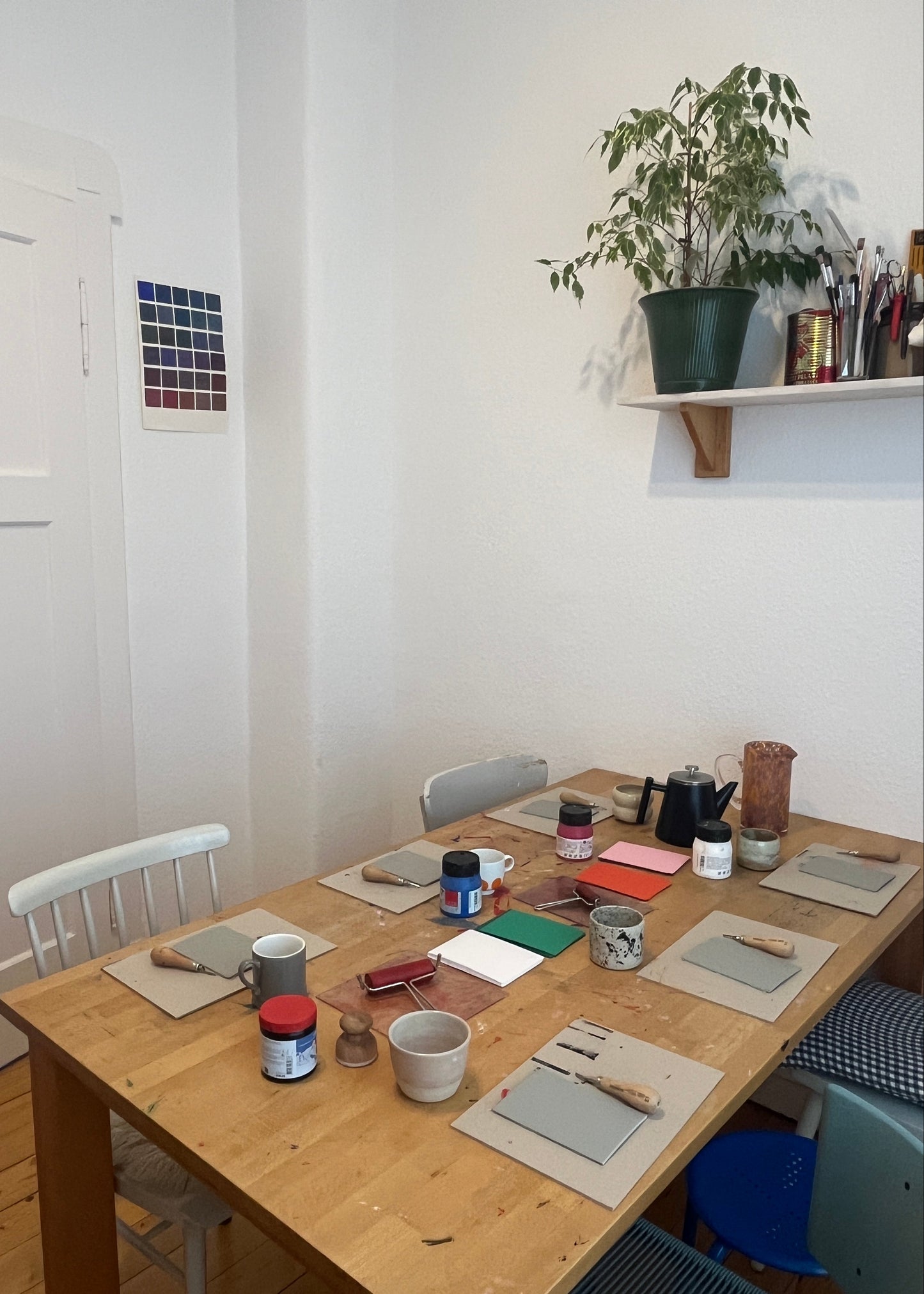 Wooden desk with various items in a room with a white wall and plant.