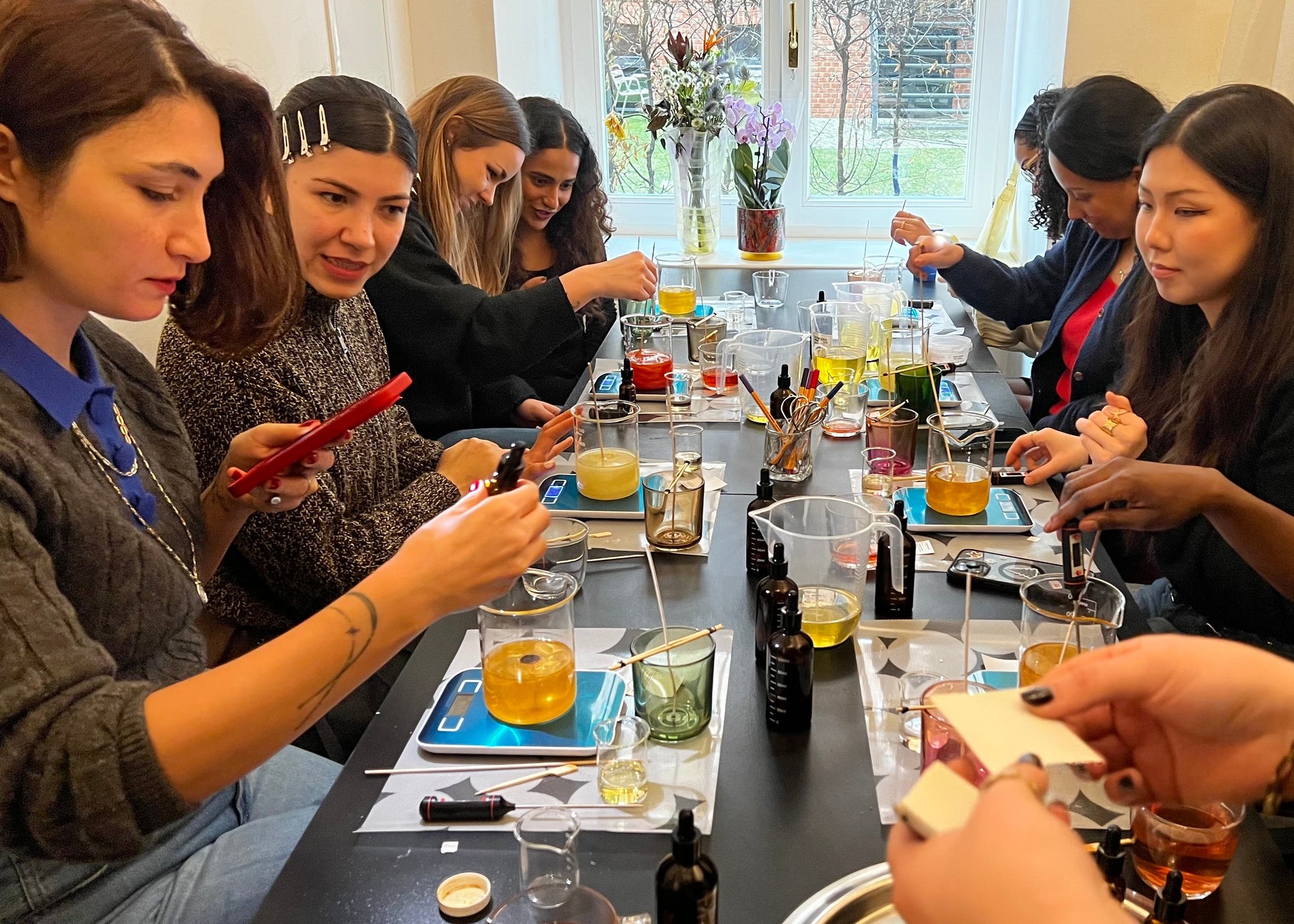 Group of people gathered around a table for a tasting event, with drinks and snacks.
