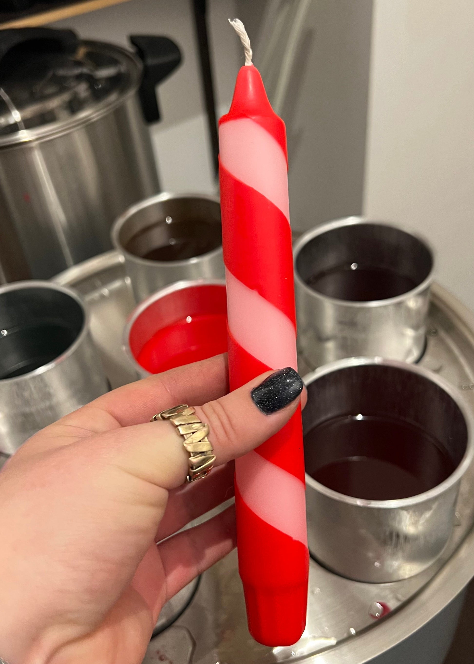 Red and white striped candle held by a hand with a gold ring, against a kitchen background.