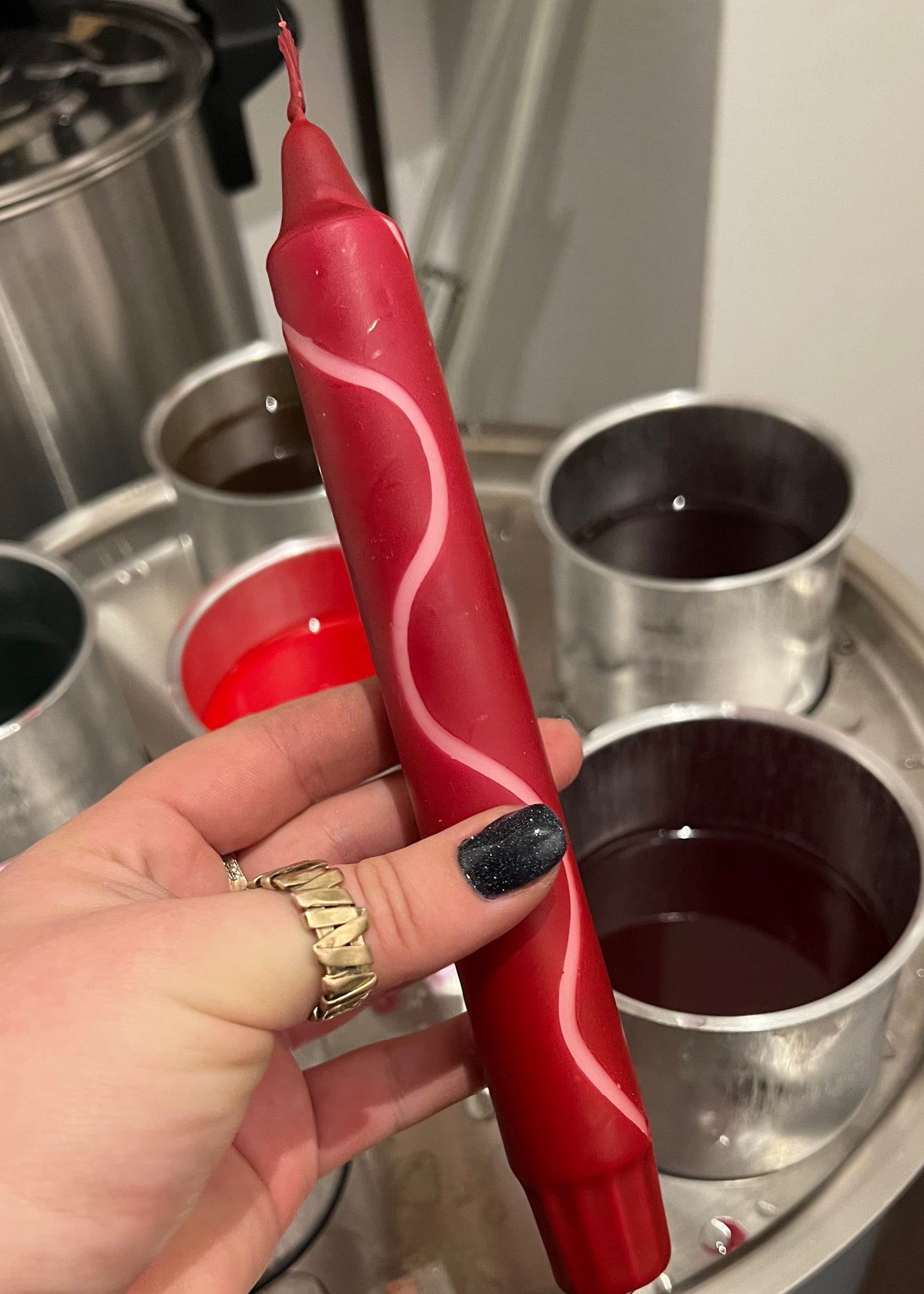 Red candle with white design held by a hand over metal containers.