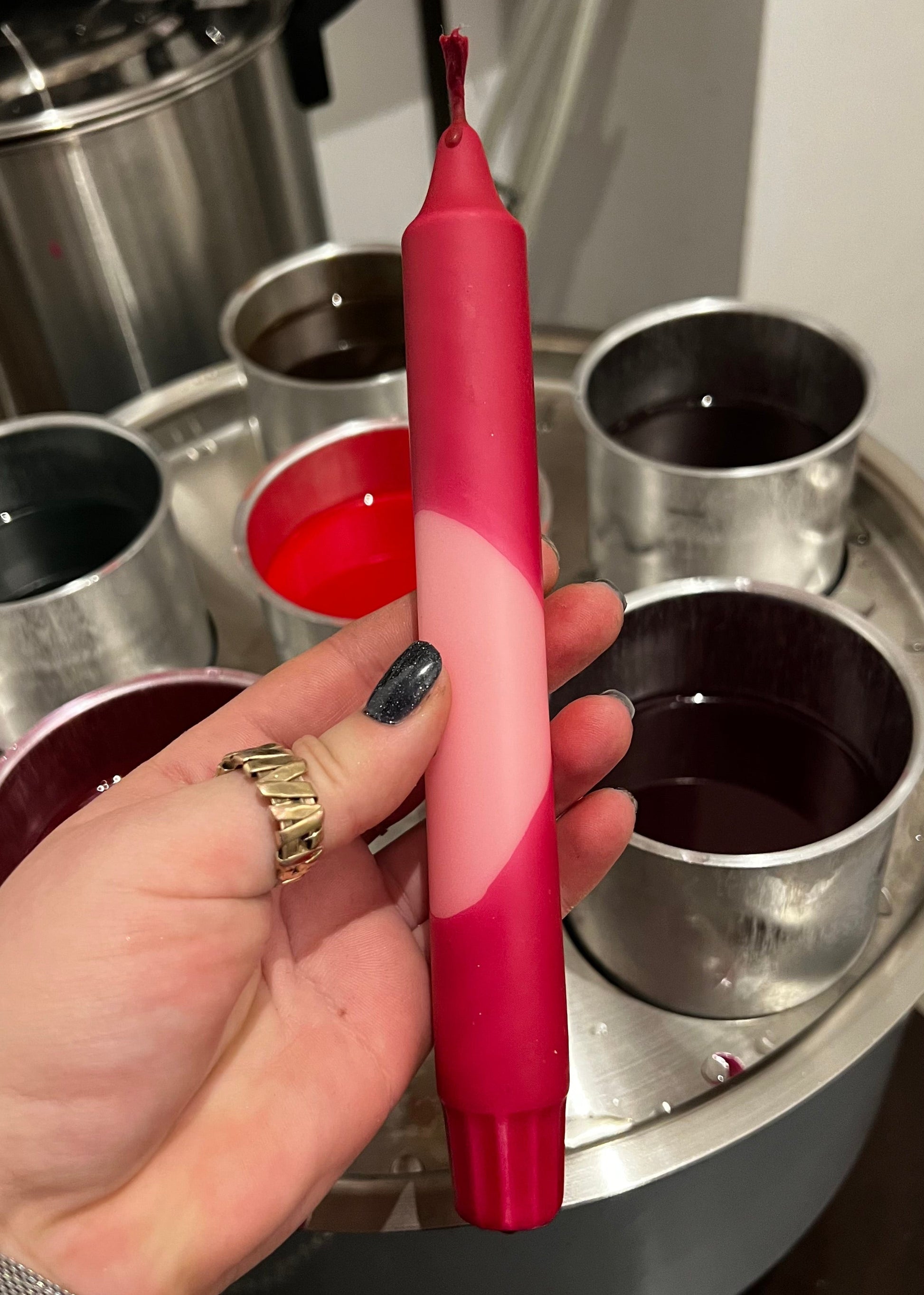 Hand holding a pink and red object with metal containers in the background