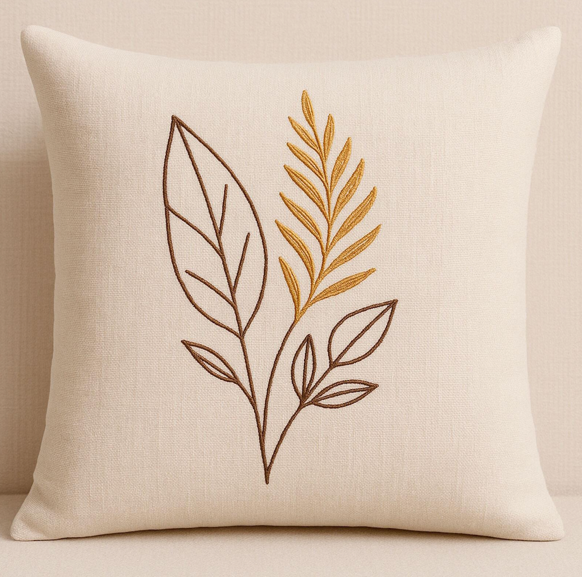 A square cream-colored throw pillow with a linen texture, featuring an embroidered botanical design of brown and gold leaves.