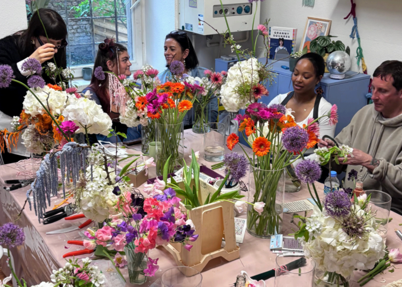 Group of people at a table with floral arrangements in a classroom setting