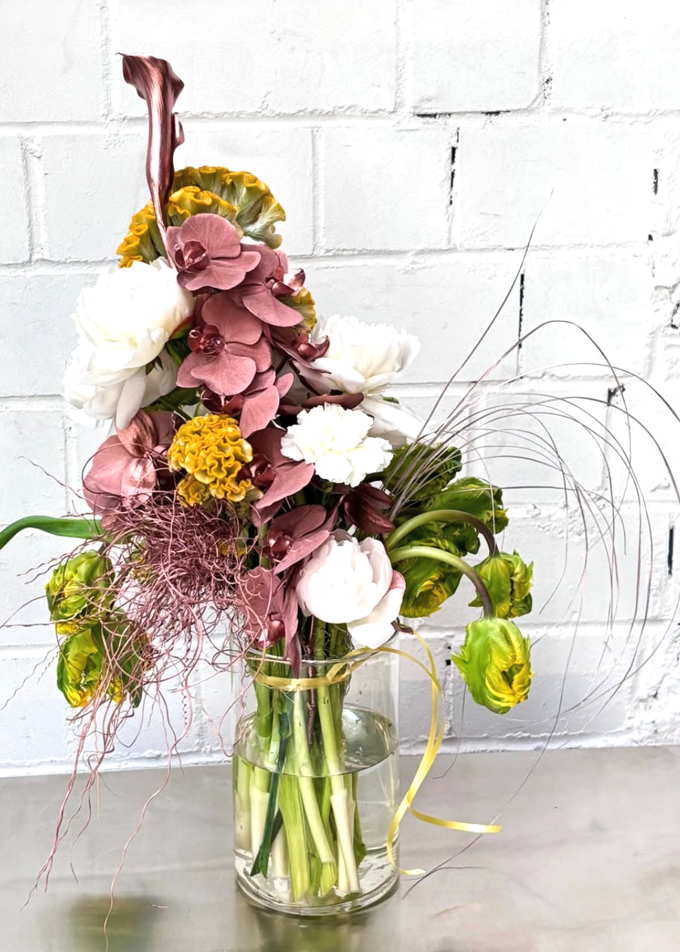 Bouquet of flowers in a clear vase against a white brick wall.